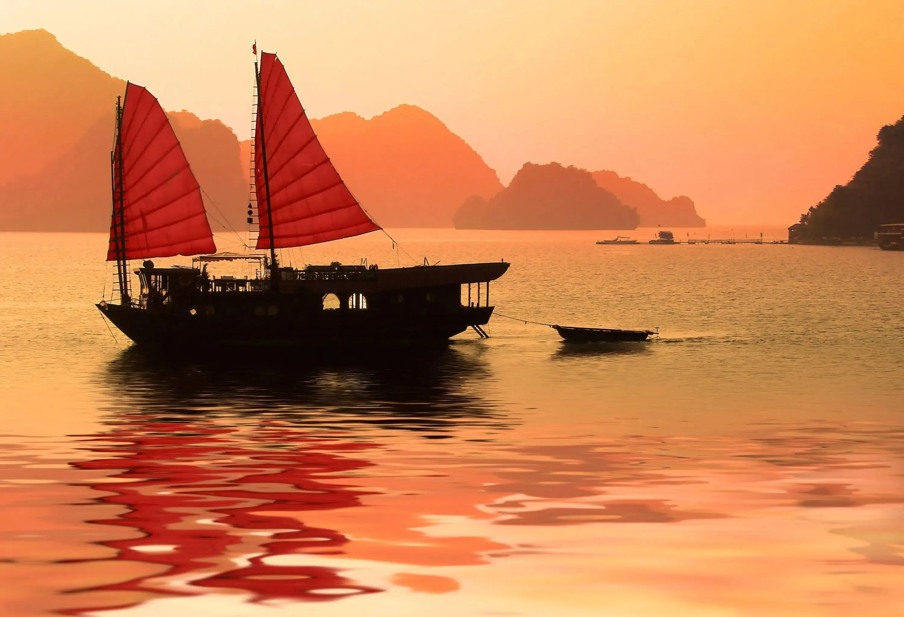 A junk boat in the sea surrounded by silhouettes of islands captured at the scenic golden hour.