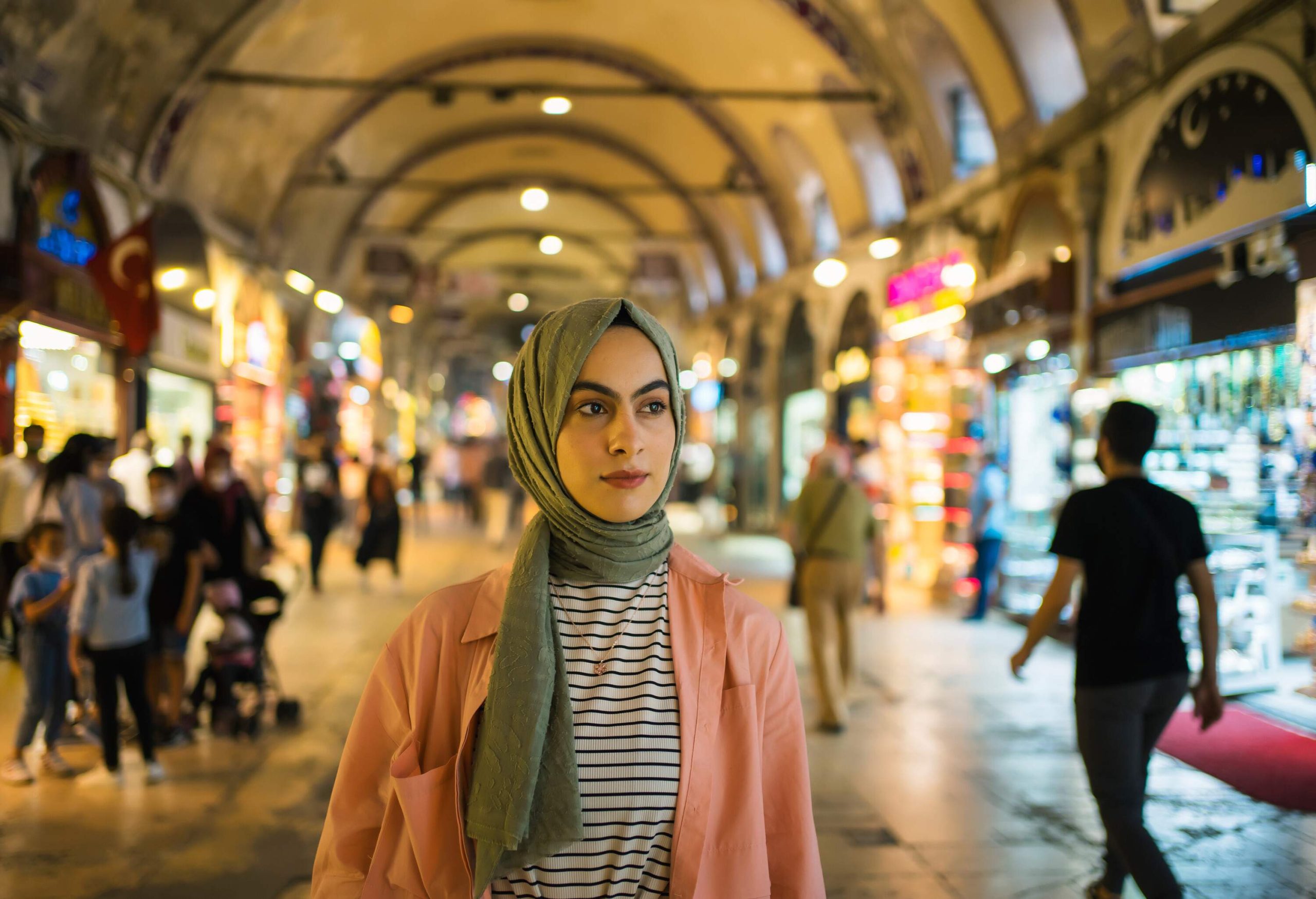 A woman in hijab against the bokeh background of a colourful indoor market.