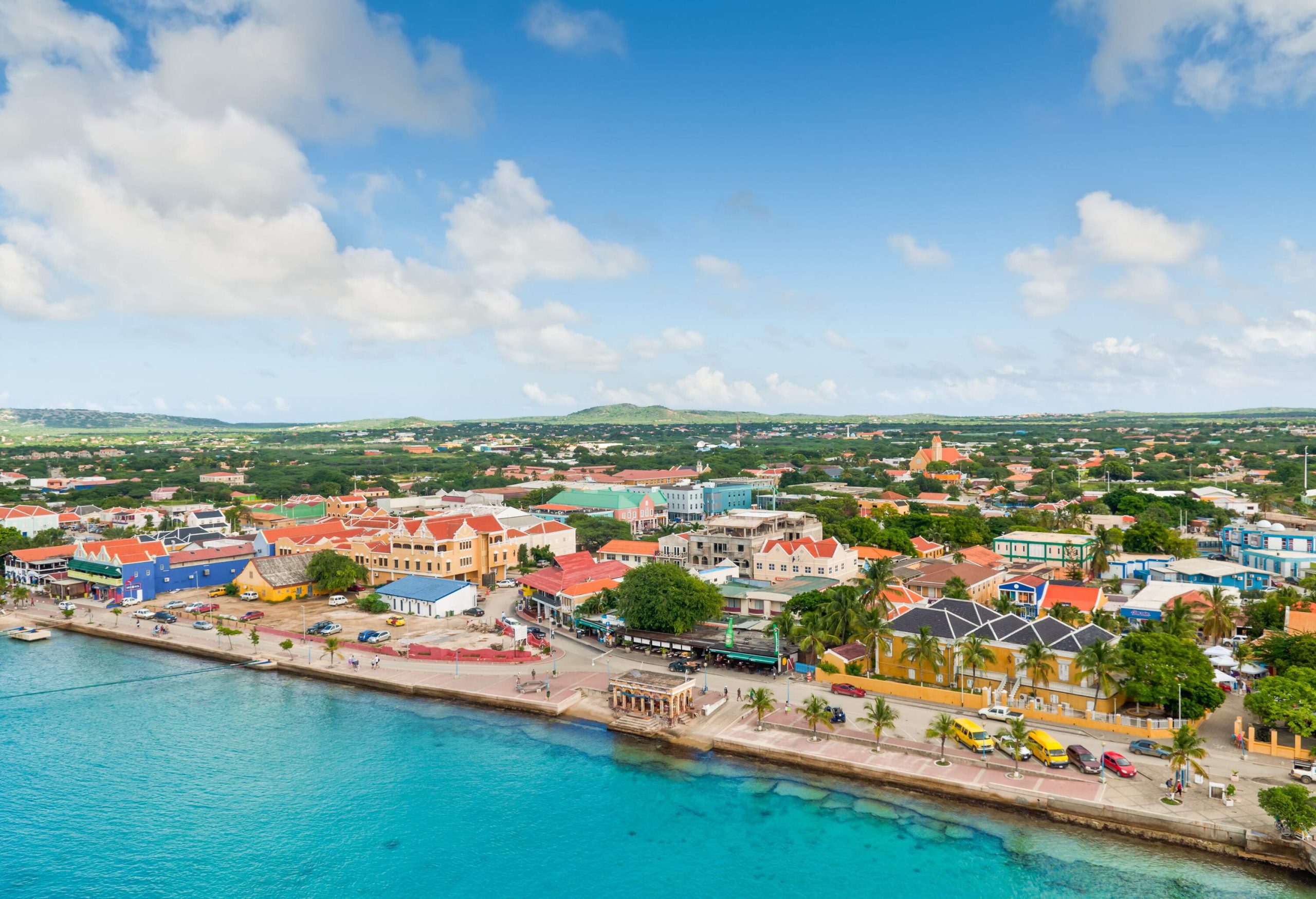 Aerial view of a colourful coastal city on a lush landscape surrounded by the sea under the cloudy blue sky.