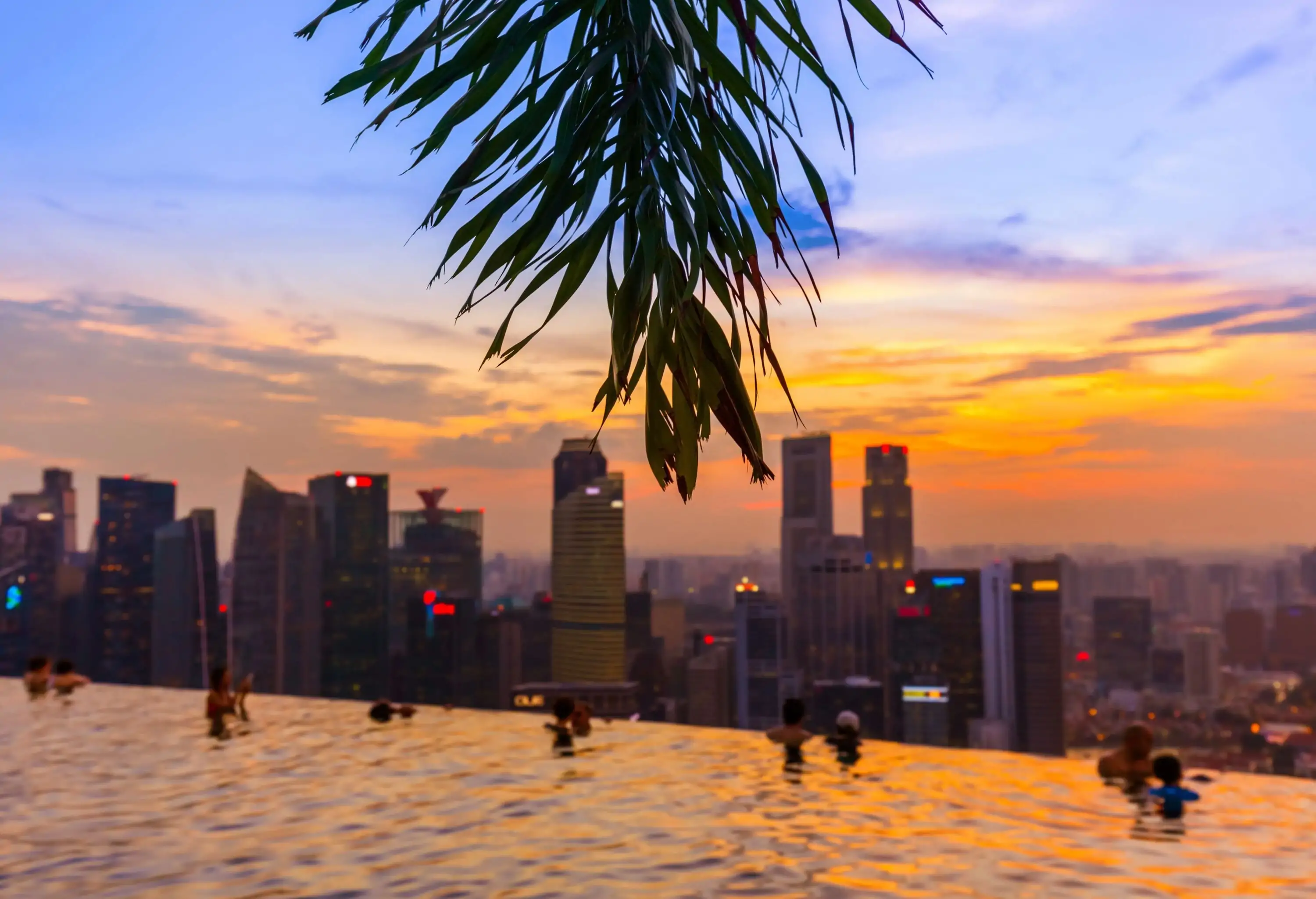 Hotel guests swim on the rooftop pool with a spectacular skyline view against the scenic sky.