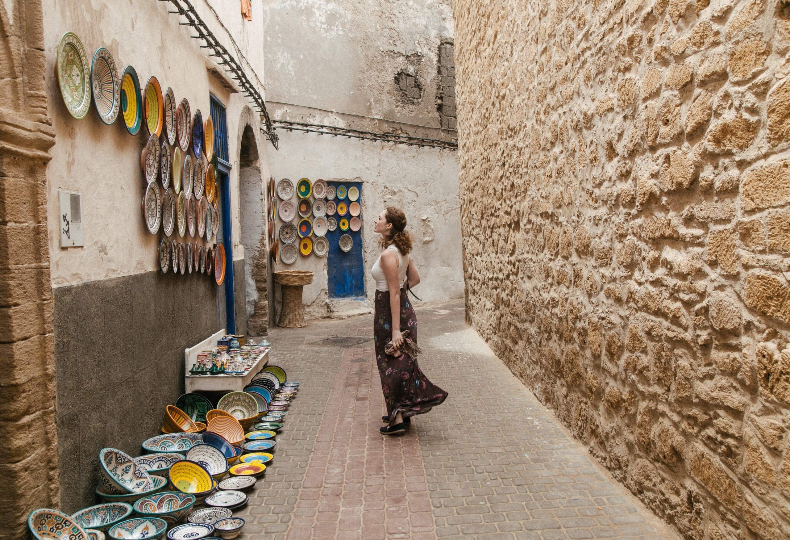 A woman in a narrow street looks at the displayed colourful ceramic plates and bowls.