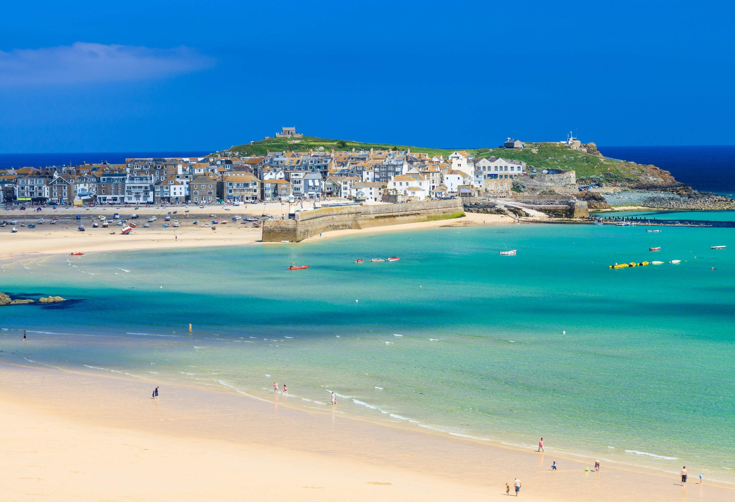 A tranquil and turquoise beach with a fine sand shore lined with classic brick houses and buildings.