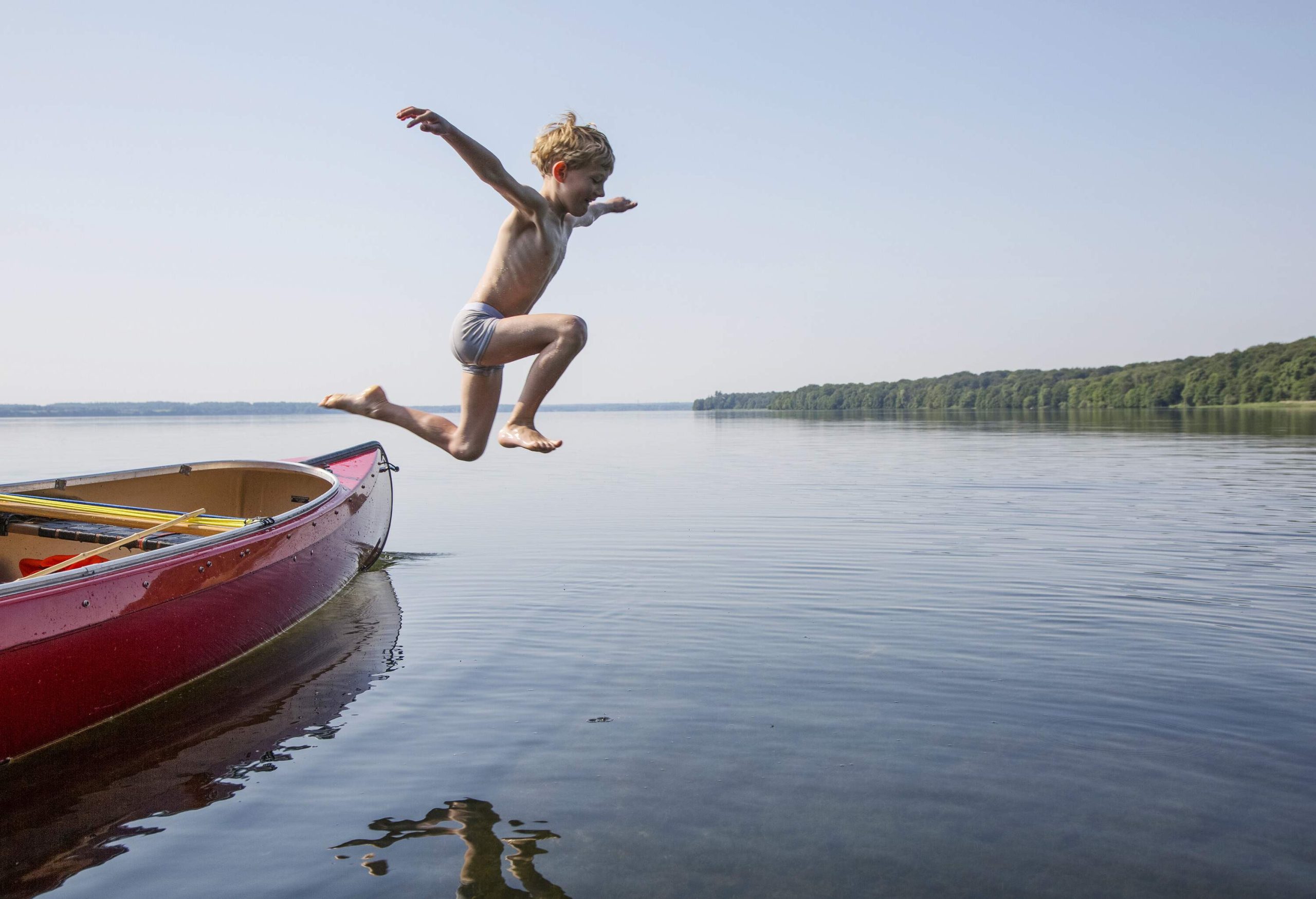 A little boy jumping into a lake from a canoe.