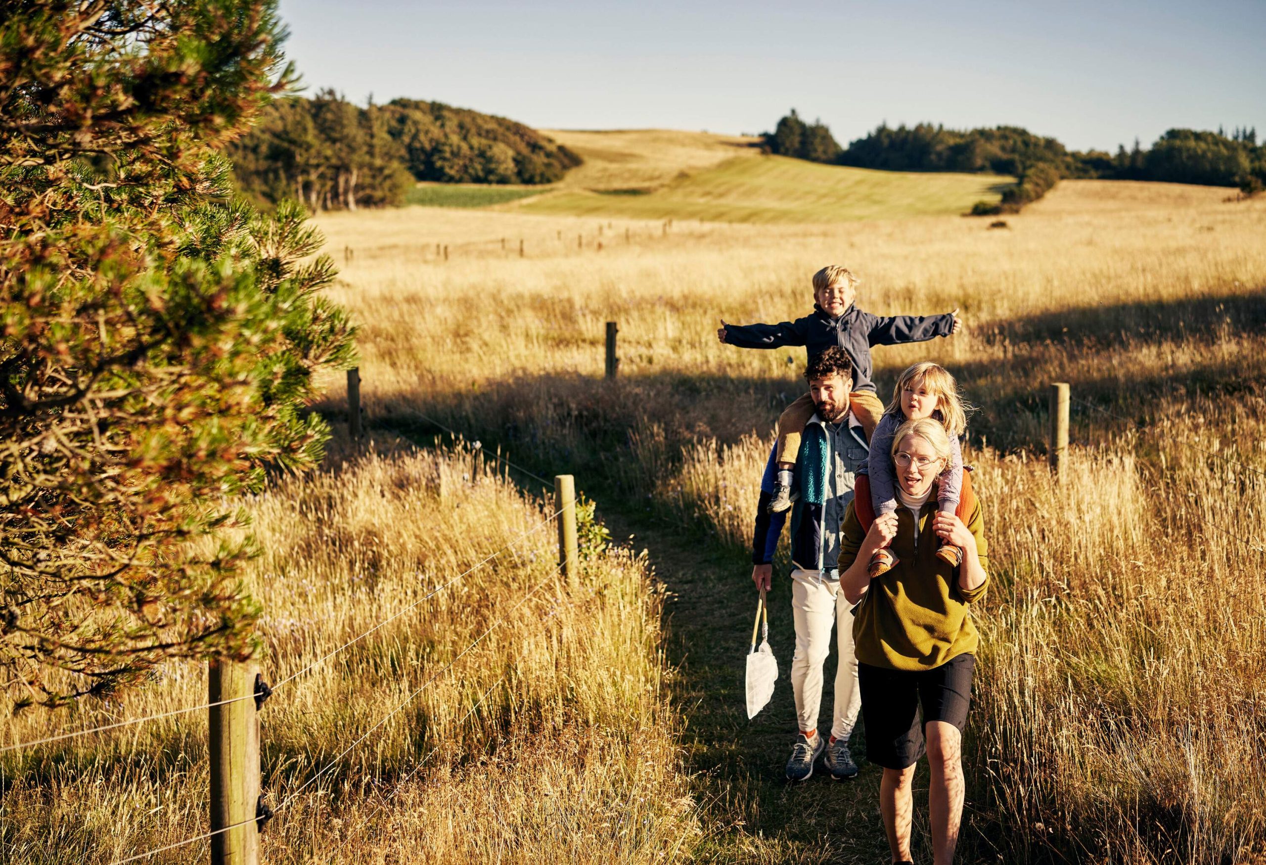 A couple walking through a grass field with their children on their backs.