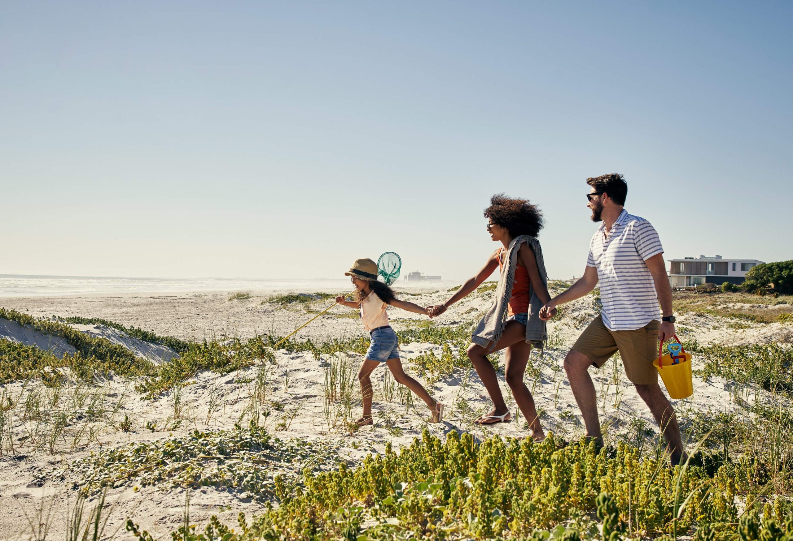 A little girl carrying a landing net leading her parents down to the beach.