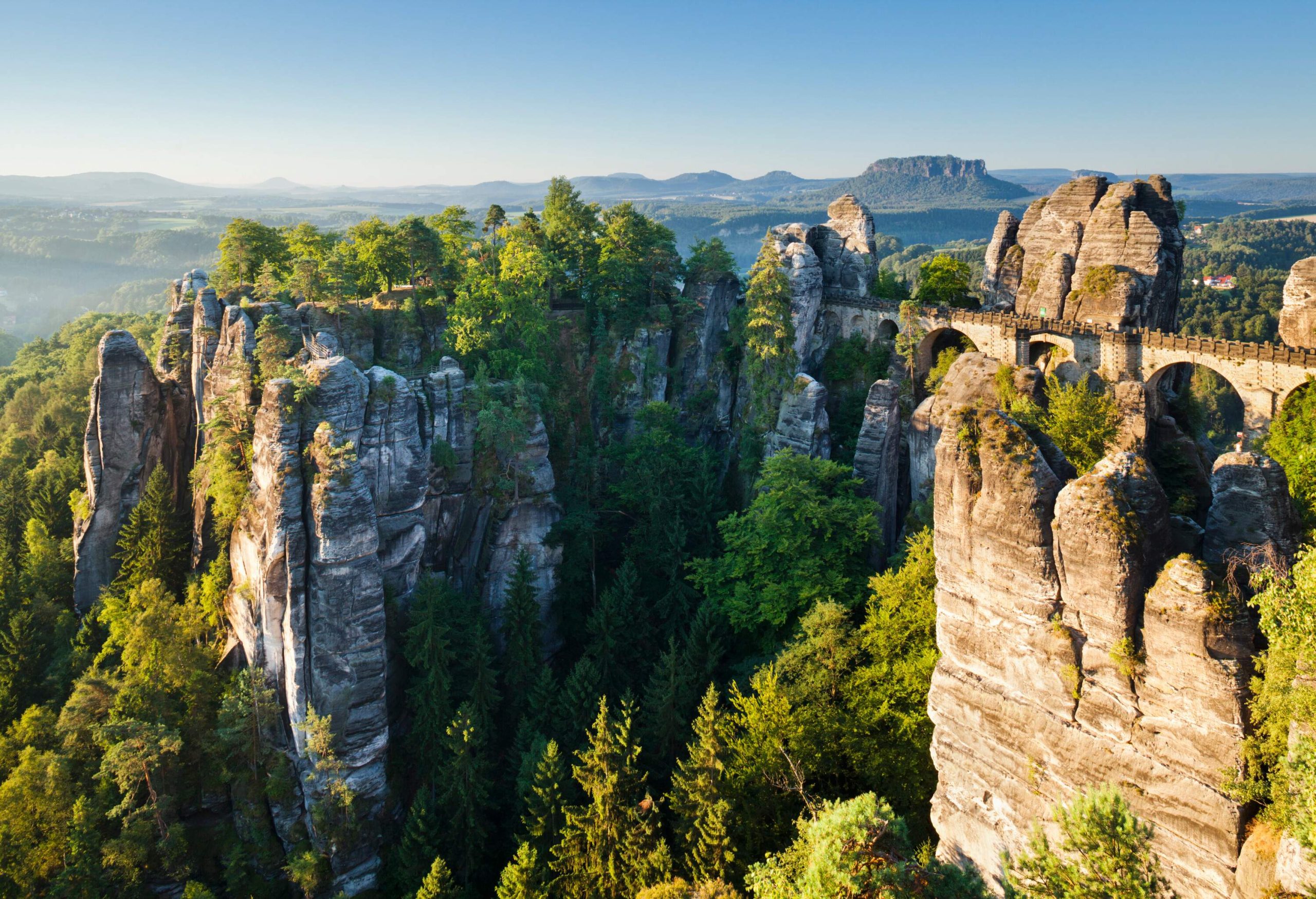 Giant fascinating sandstone rock formations surrounded by tall trees with a long bridge connecting several rocks.