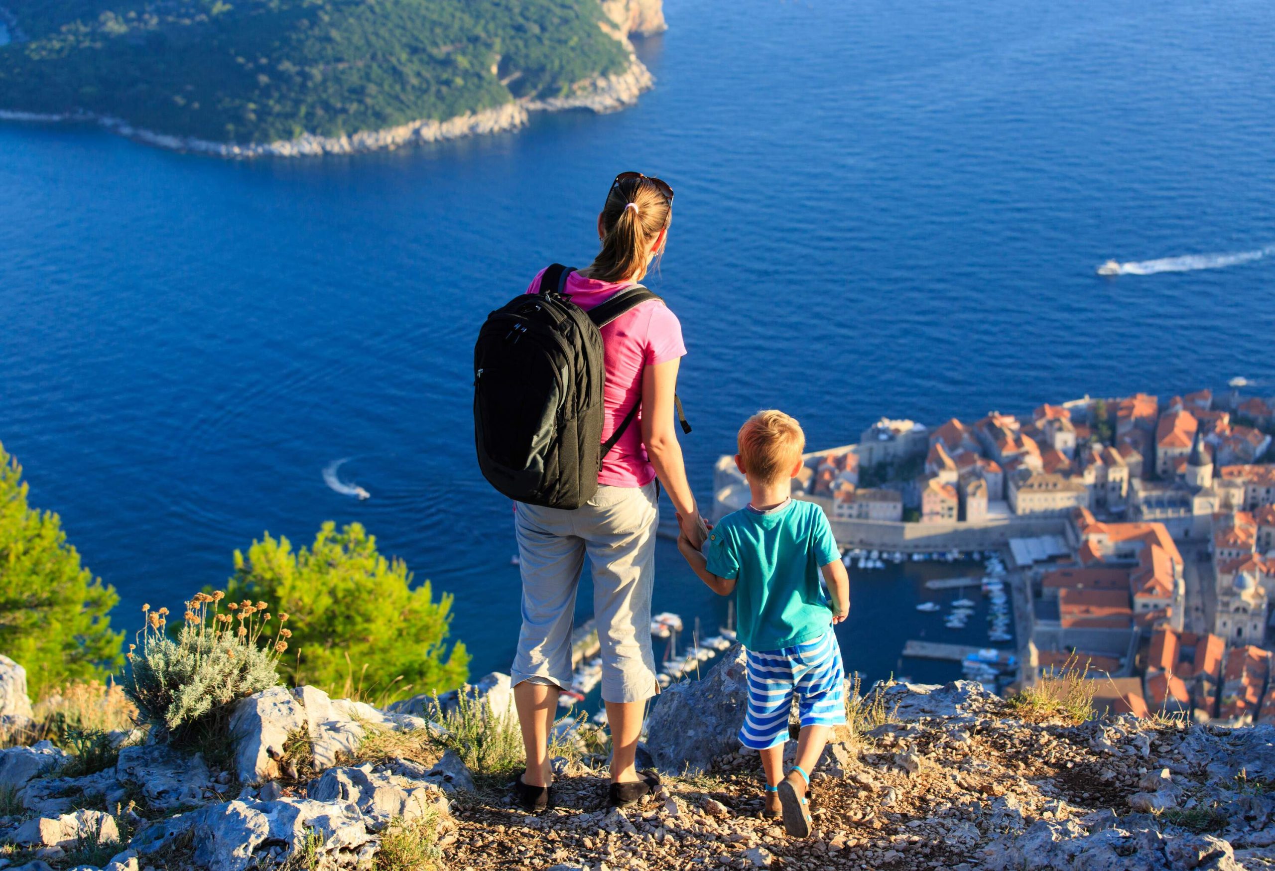 A woman and a small boy standing on the edge of a hill overlooking the sea and harbourfront buildings.