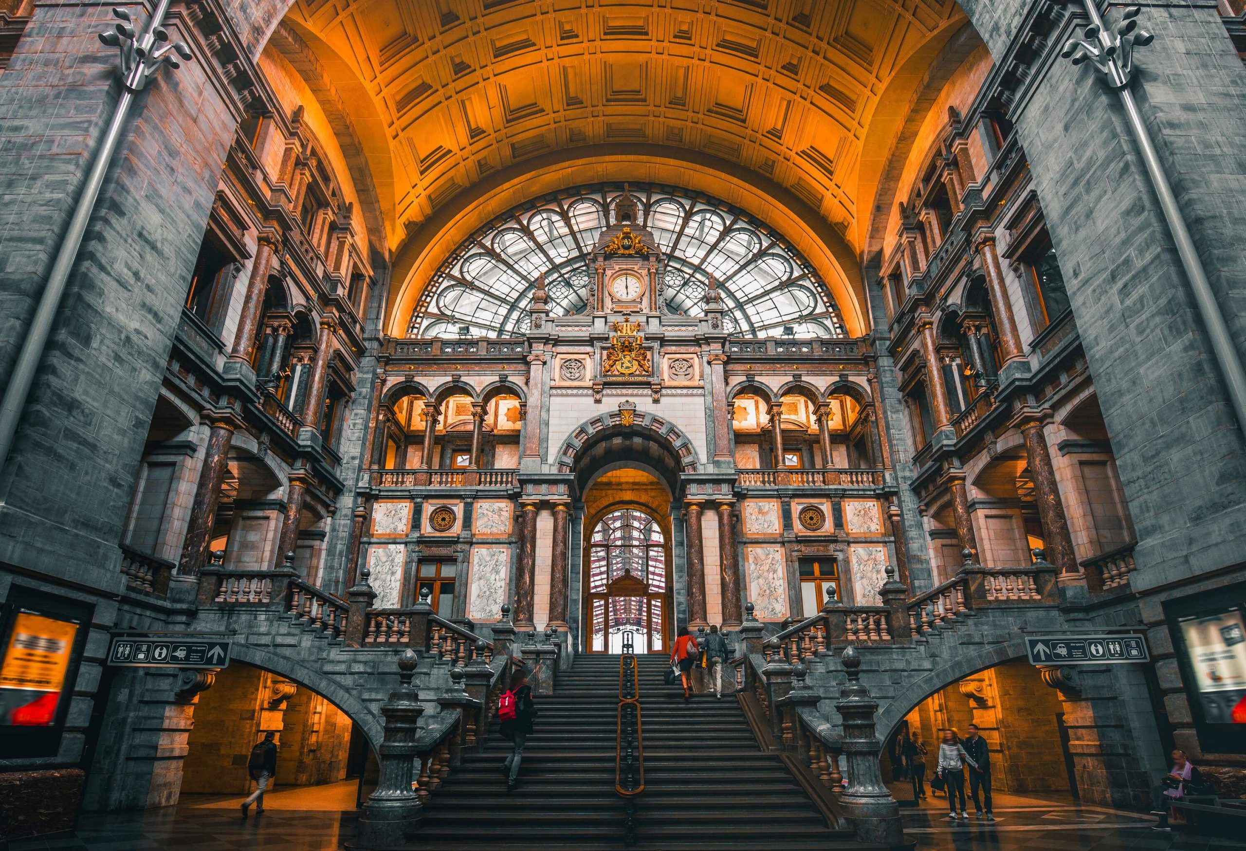 Antwerpen-Centraal railway station's glorious interior, with people climbing up the stairs and walking through the halls.