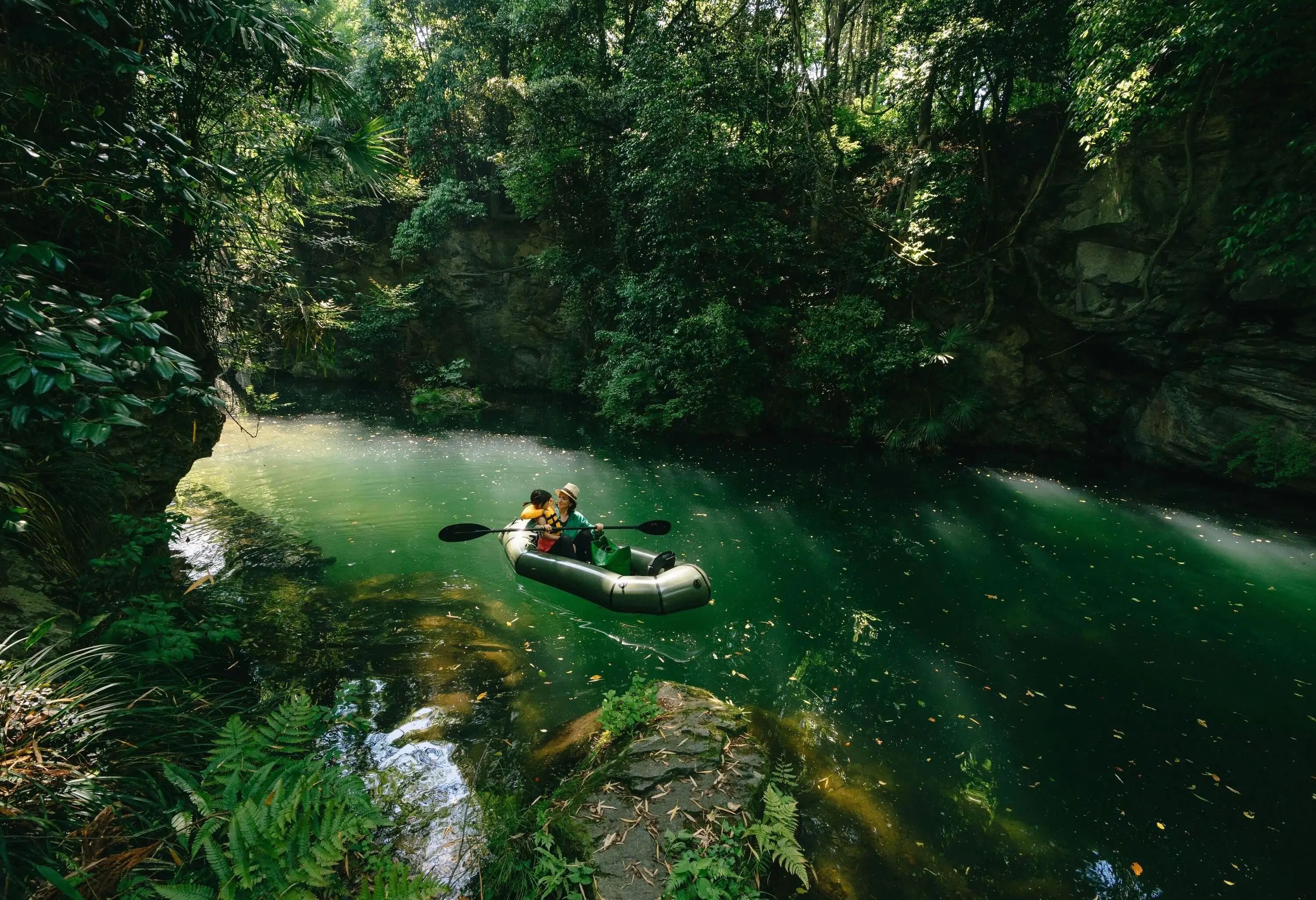 Mother and child in a packraft boat on a scenic and lush green river.