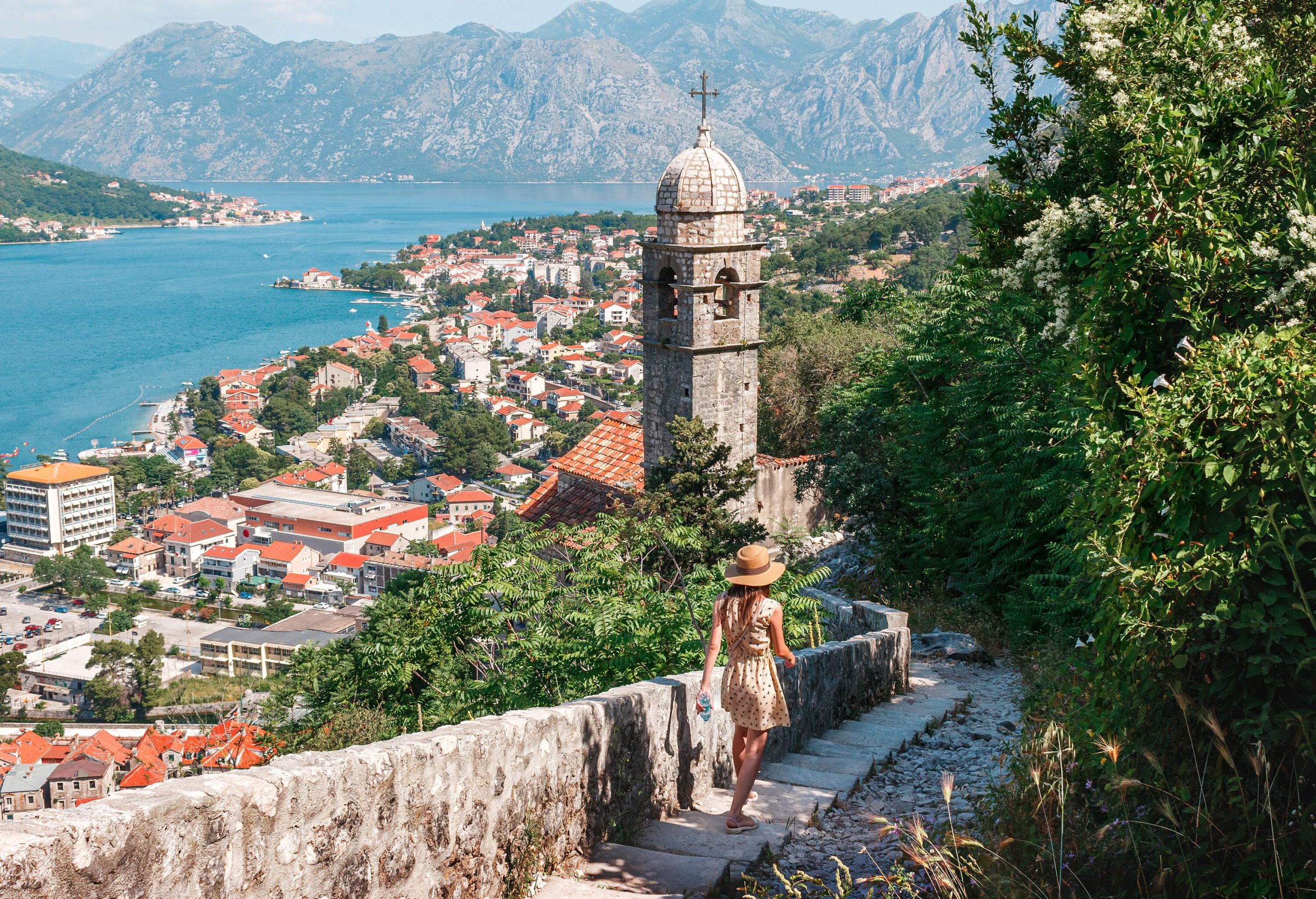 A lady tourist on the downhill staircase approaching a church bell tower overlooking the cityscape.