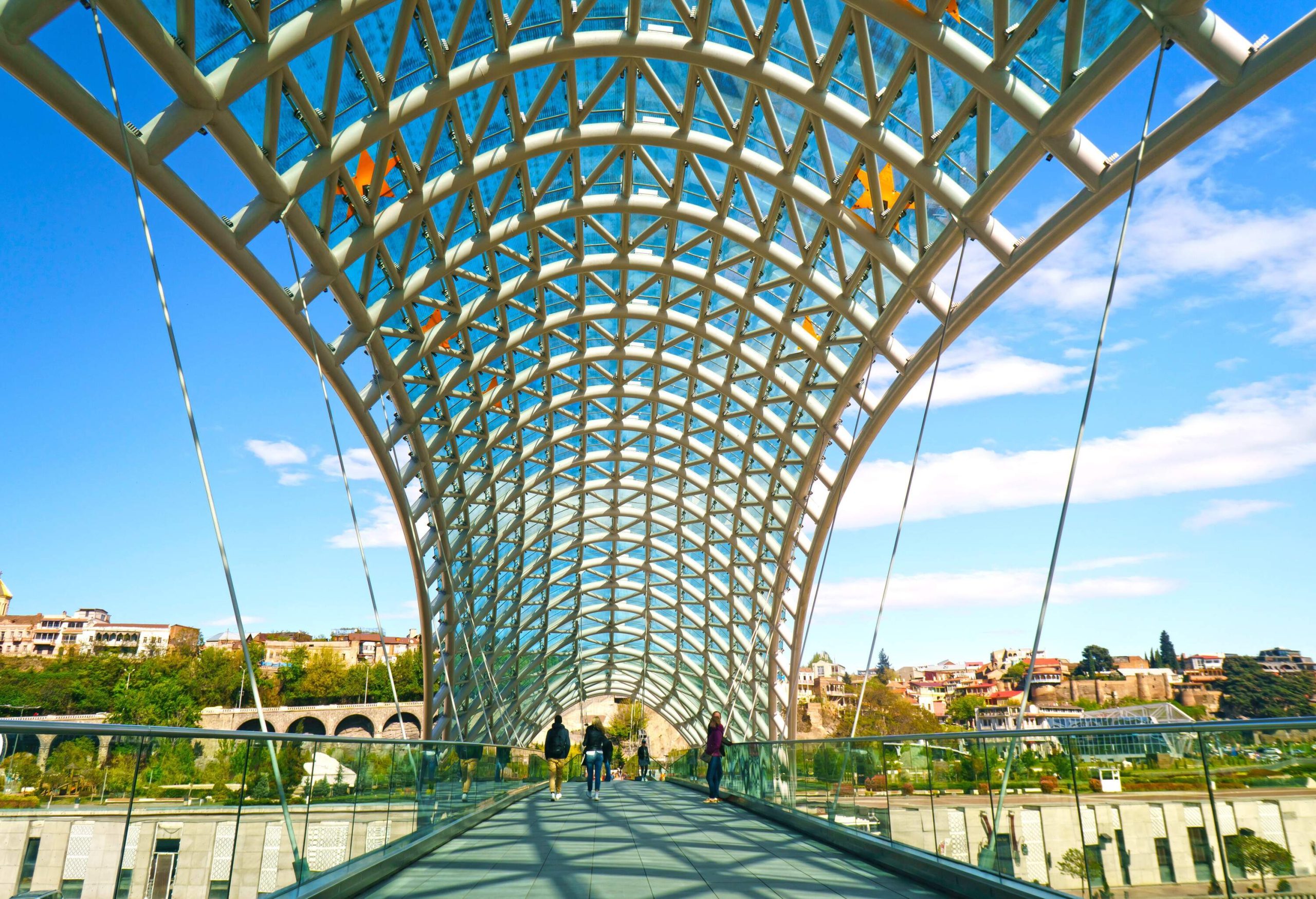 A modern and distinctive pedestrian bridge of steel and glass spans over the river, showcasing a unique and contemporary design.