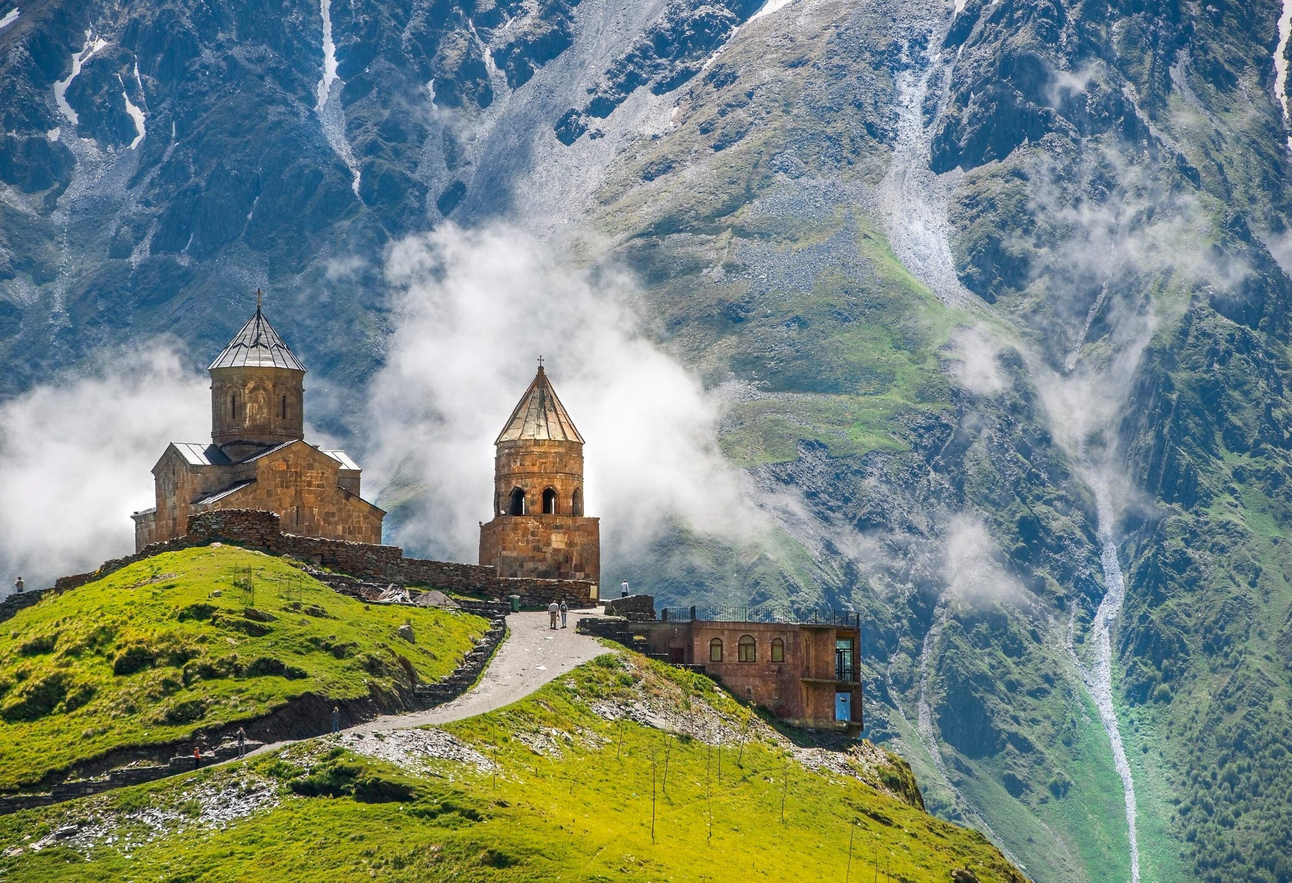 The Gergeti Trinity Church, dating back to the 14th century, showcases a distinct conical roof and stands alongside a separate bell tower atop a high mountain, offering breathtaking views of the surrounding mountainous landscape.