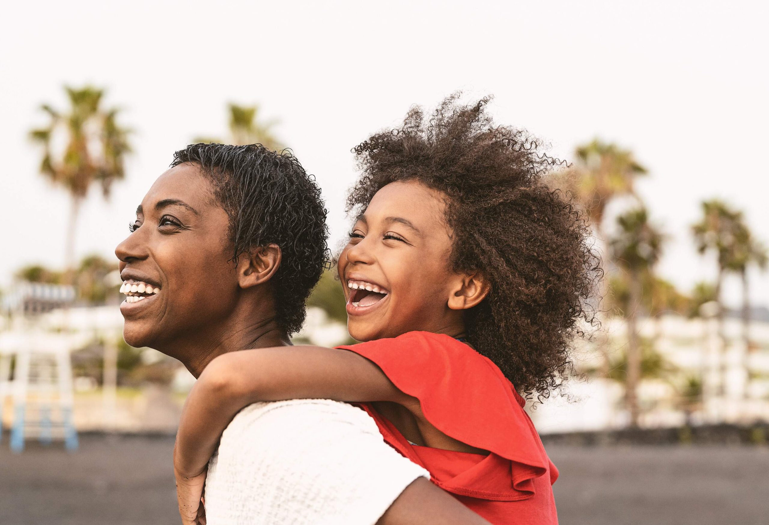 A mother giving her daughter a piggyback ride by the beach.