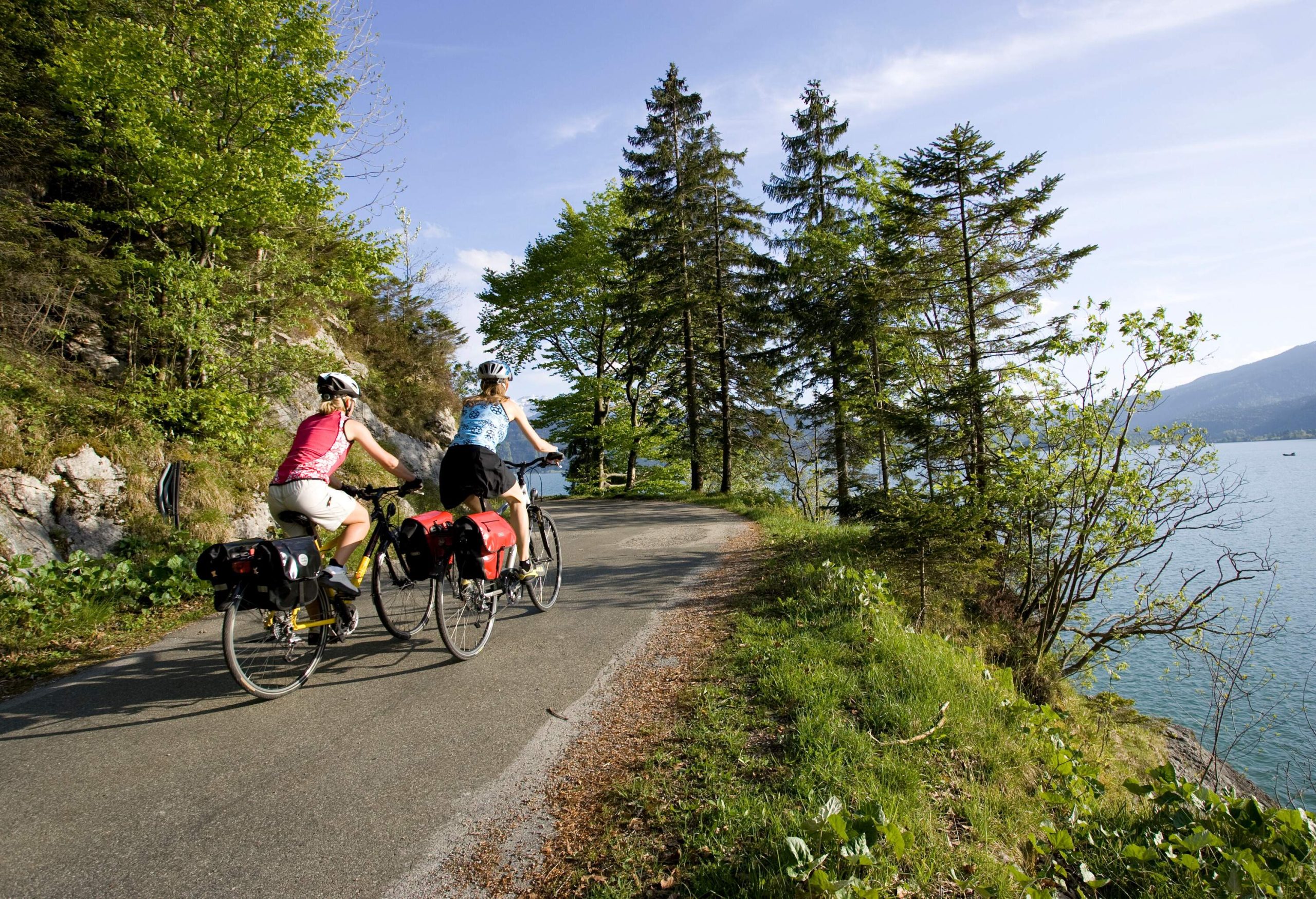 Two people riding their bikes on an uphill road in the mountains overlooking a lake.