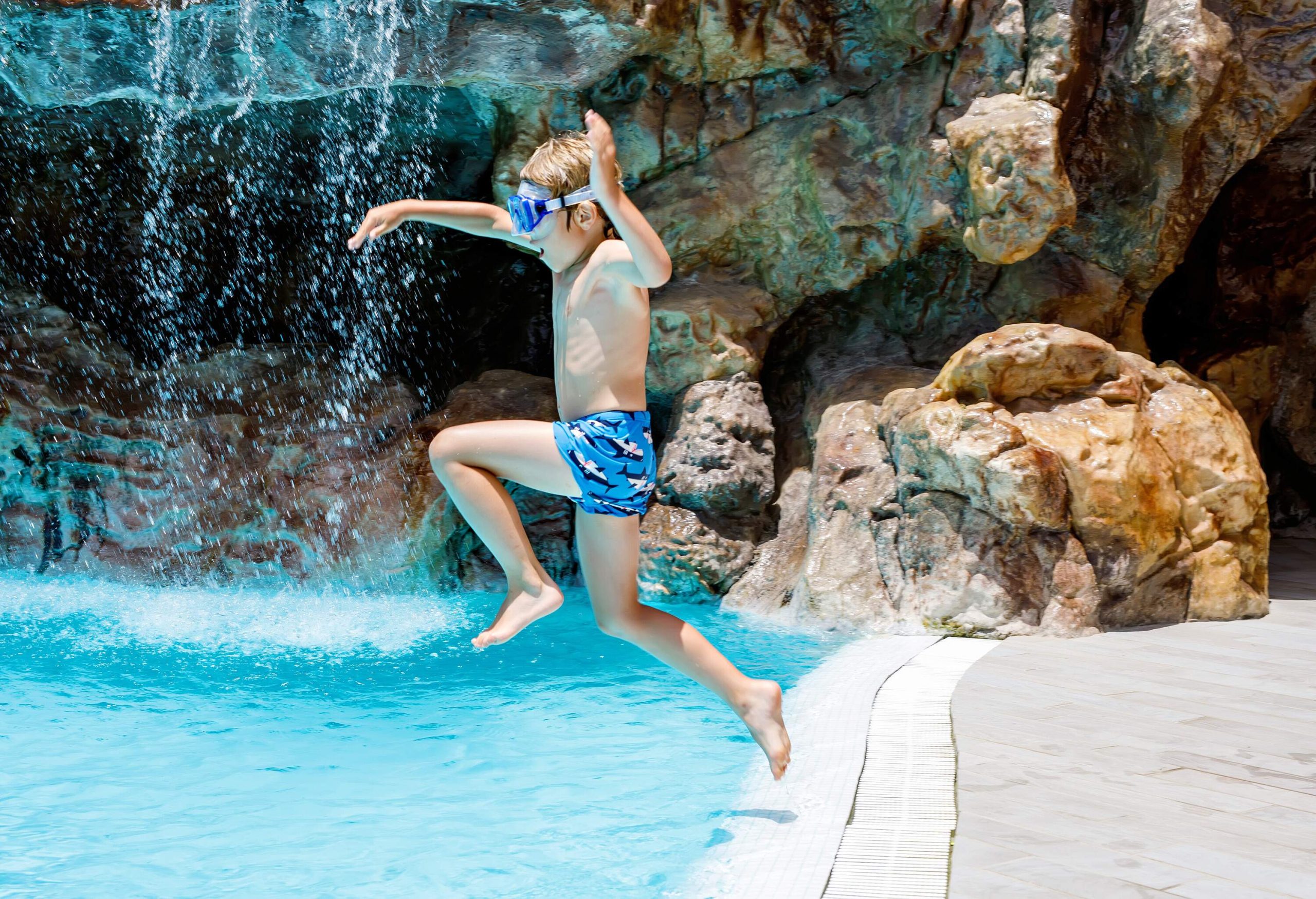 A boy with goggles jumps above a pool.