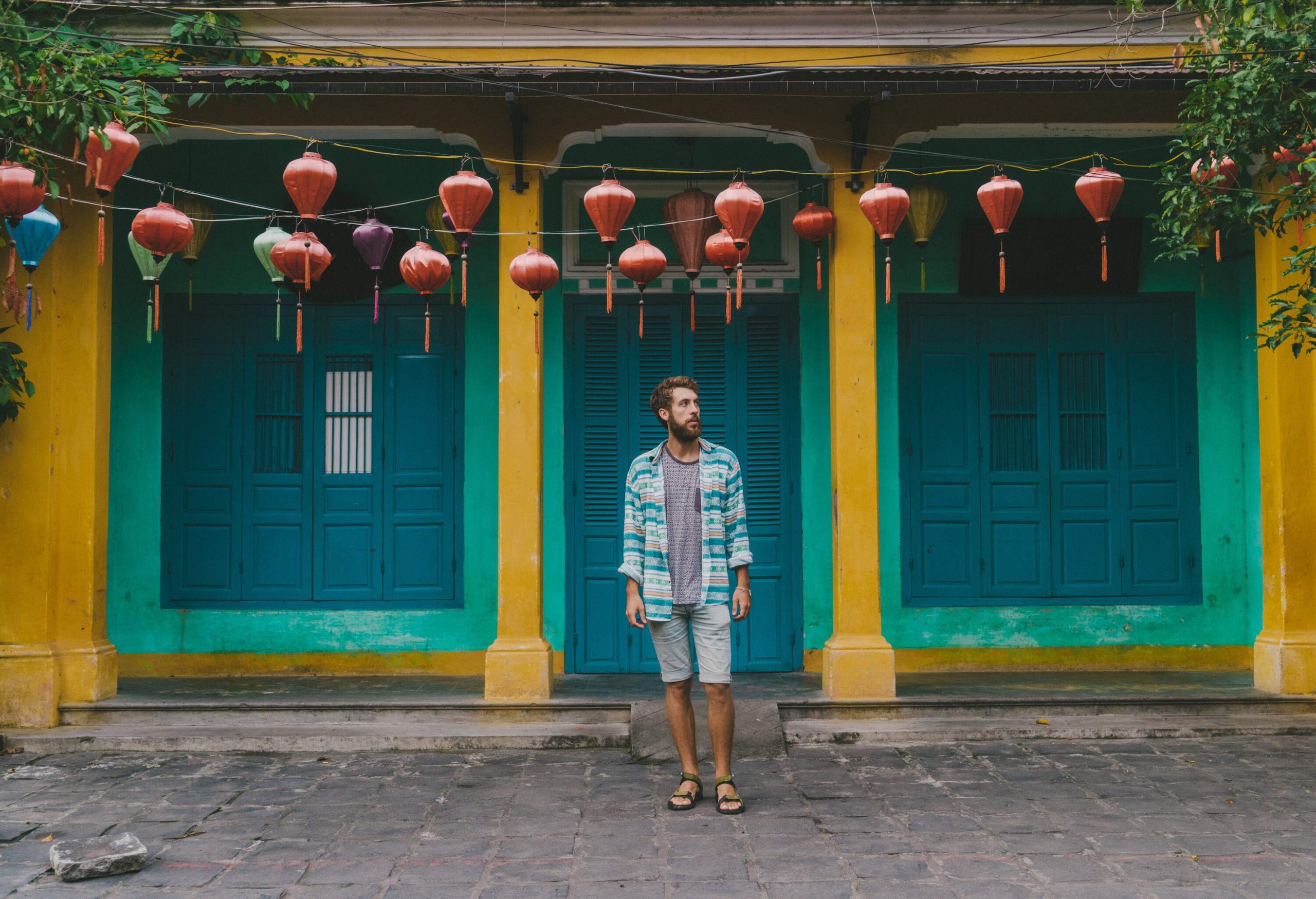 A man stands against a colourful classic house adorned with hanging lanterns.