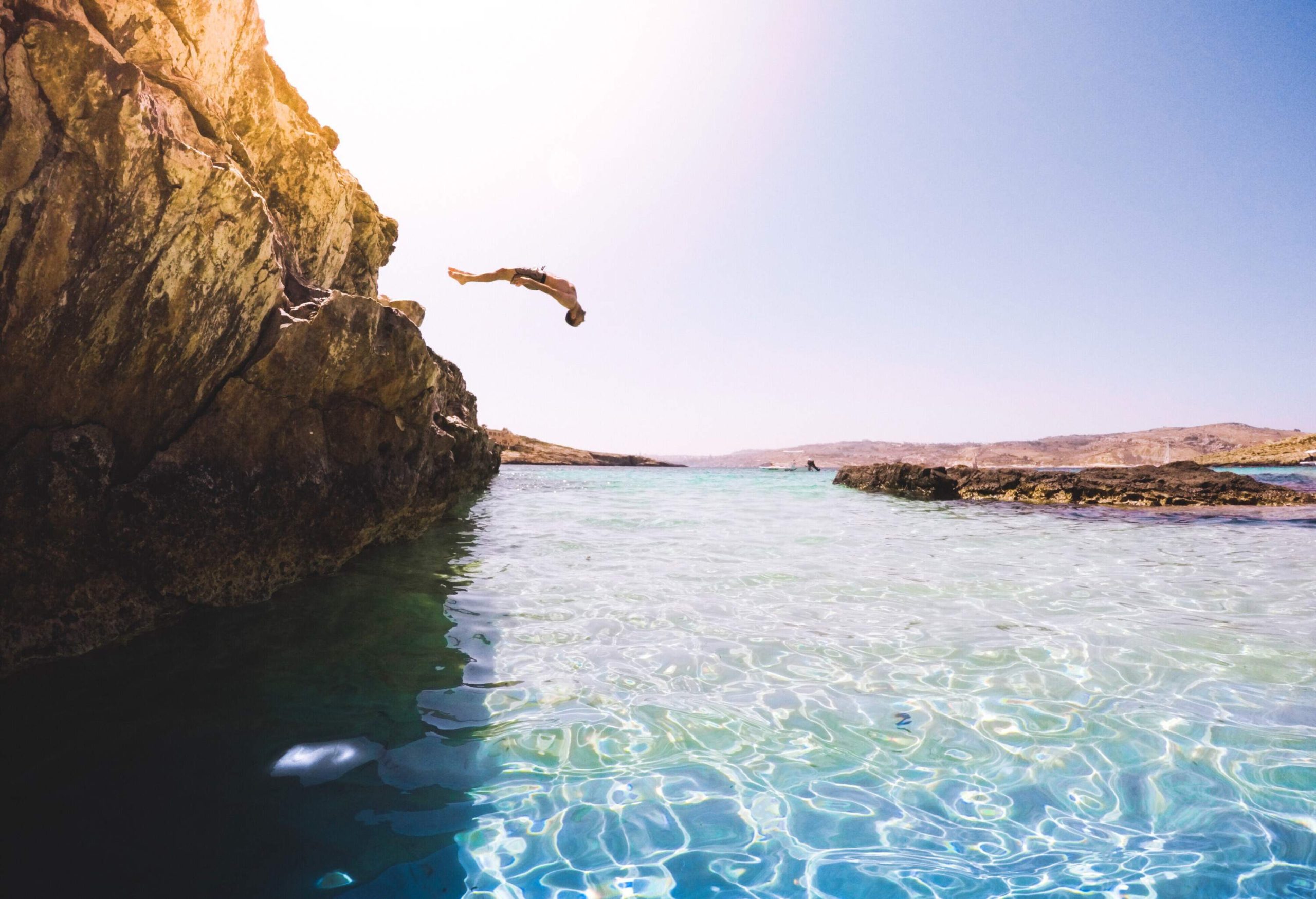 A man diving backwards into the sparkling sea from a cliff.