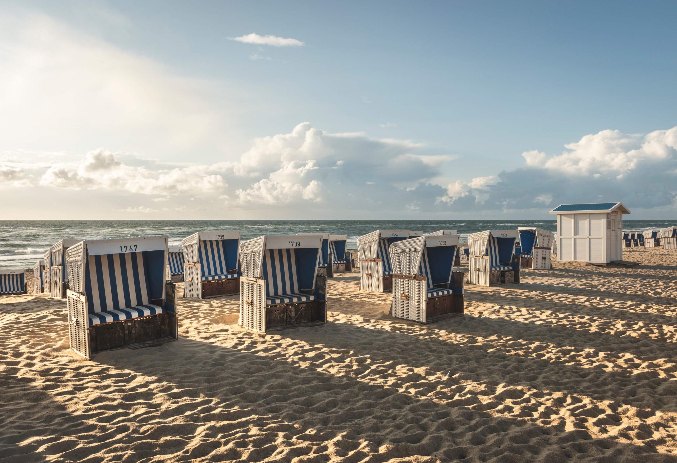 Numerous white and blue stripe hooded beach chairs lined on a fine sand beach.