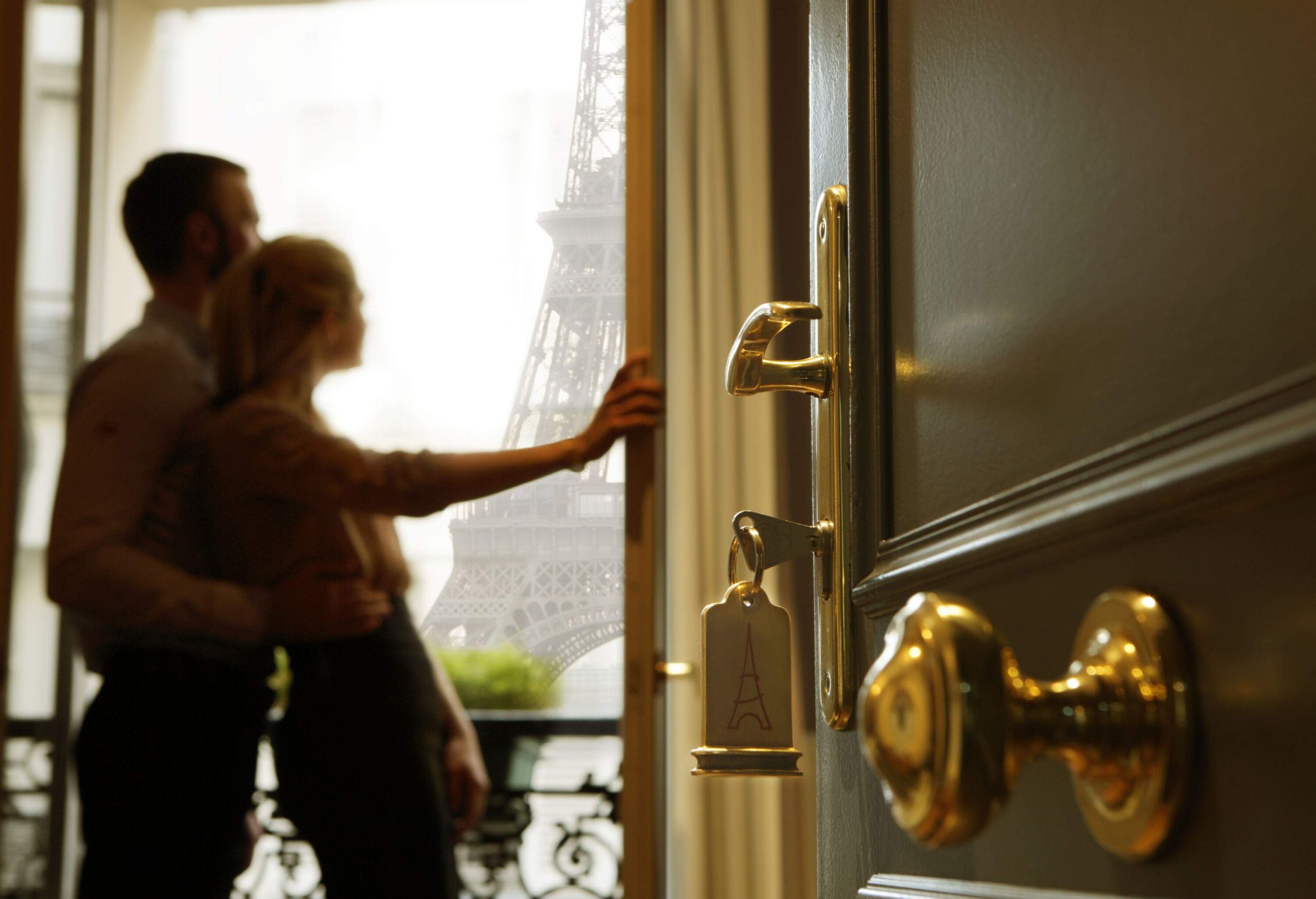 A couple on a glass window of a hotel room viewing the Eiffel tower.