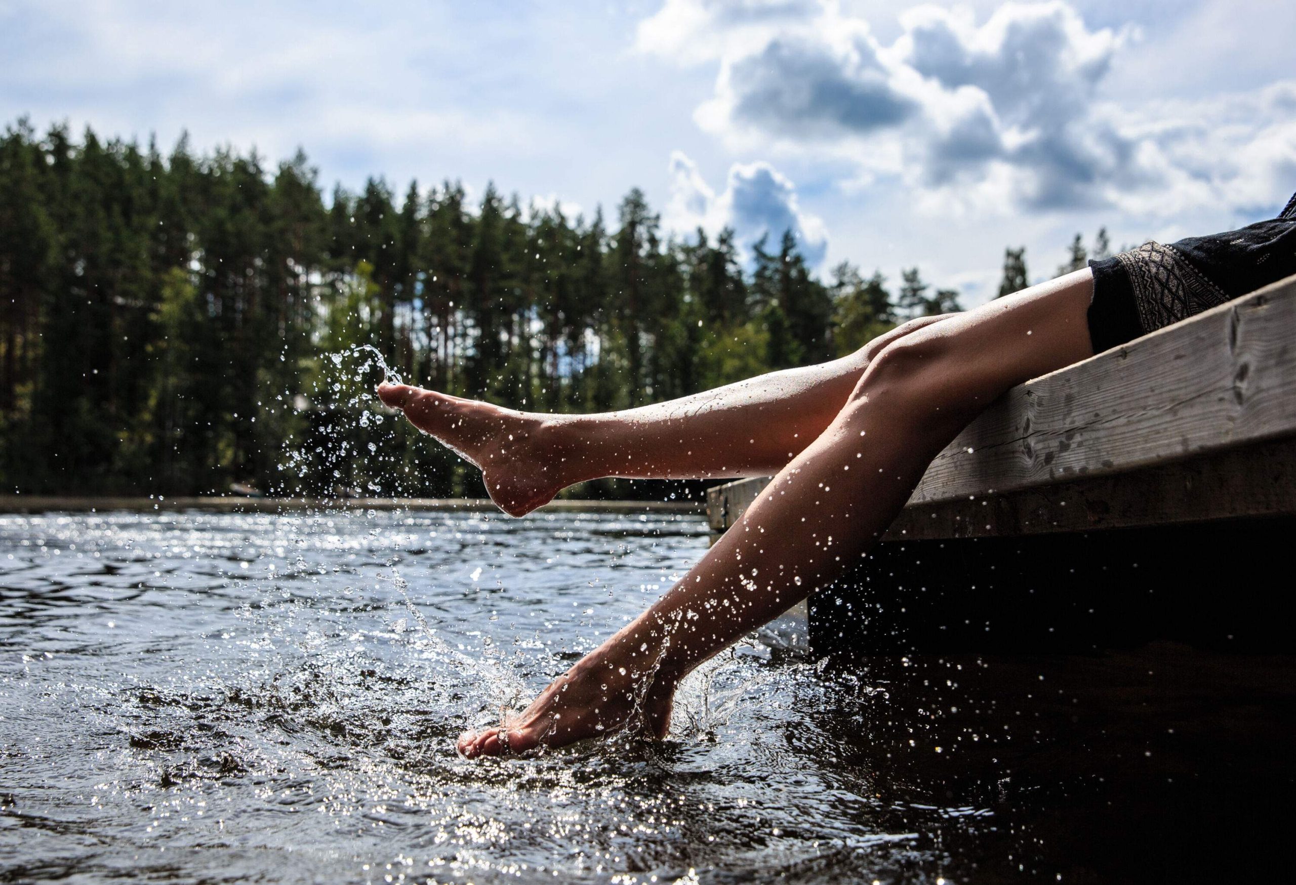 A person sitting on a dock and splashing water with their legs in the lake.