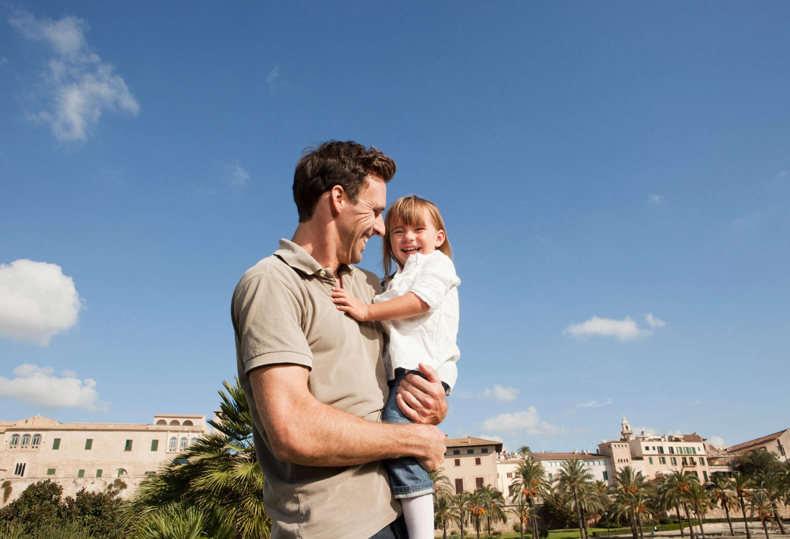 A man carries a kid as they both smile at each other.