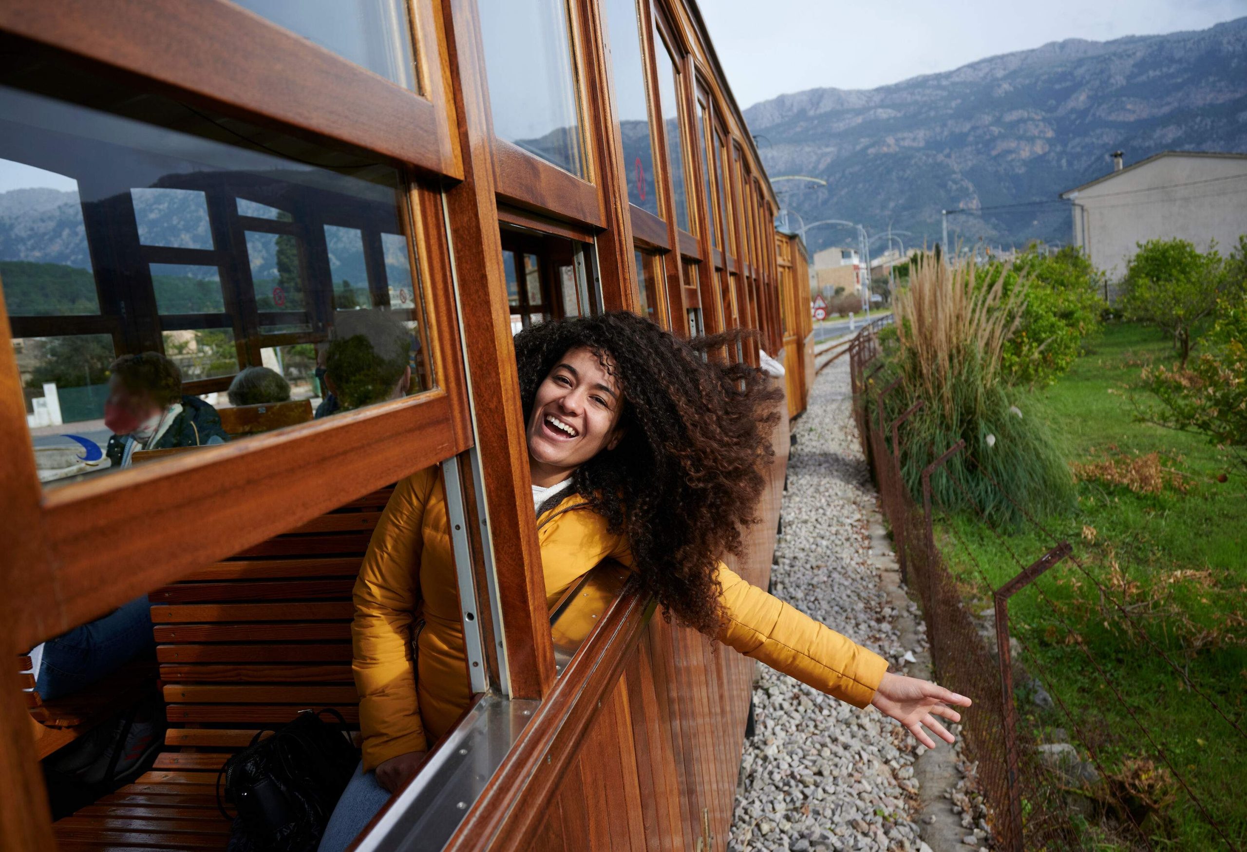A happy woman with beautiful long curly hair peeking her head out of a train window.