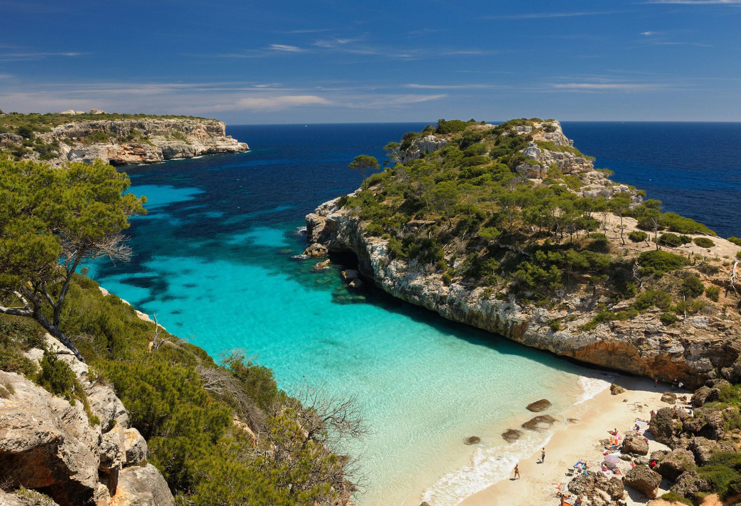 A shallow sandy beach with clear and tranquil waters along steep rocky cliffs.
