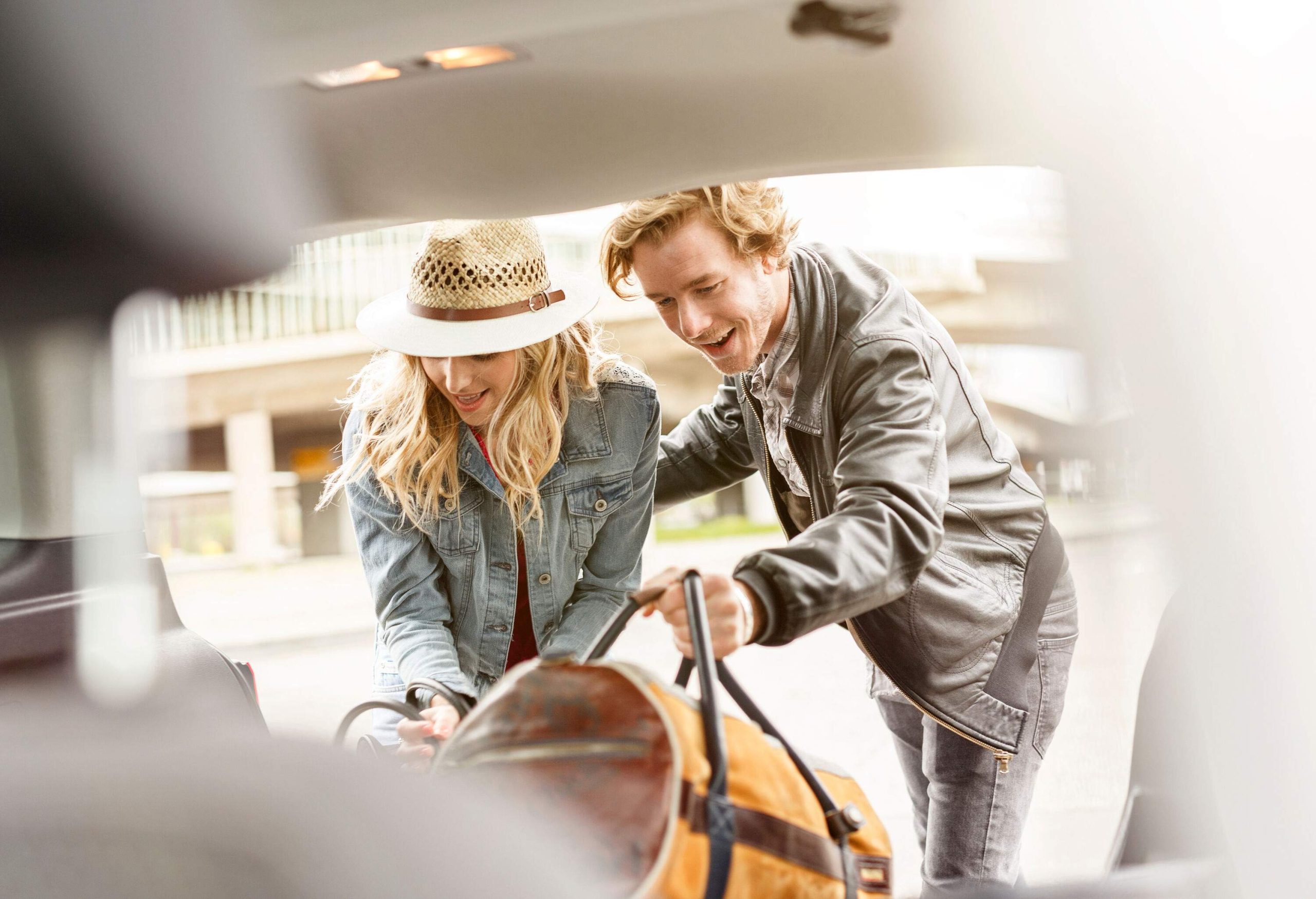 A couple in casual clothes loading bags into a car's trunk.