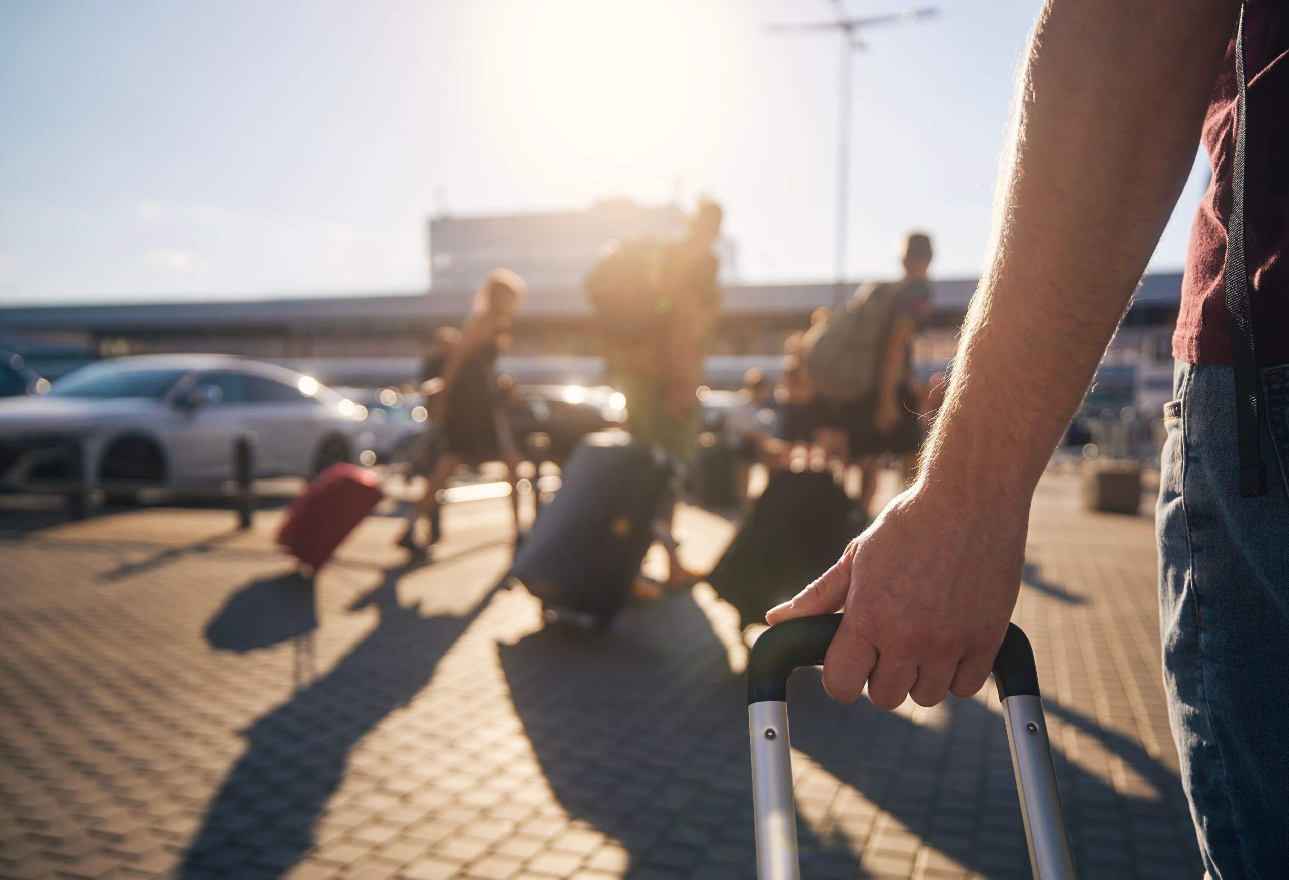 Group of people walking to airport terminal at summer sunset. Selective focus on hand of man with suitcase.