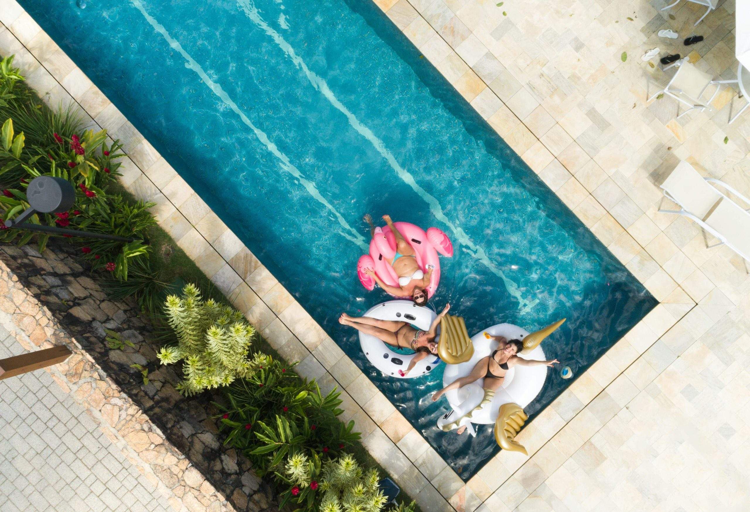 Three women lounging on uniquely-shaped pool floats in a rectangular swimming pool.