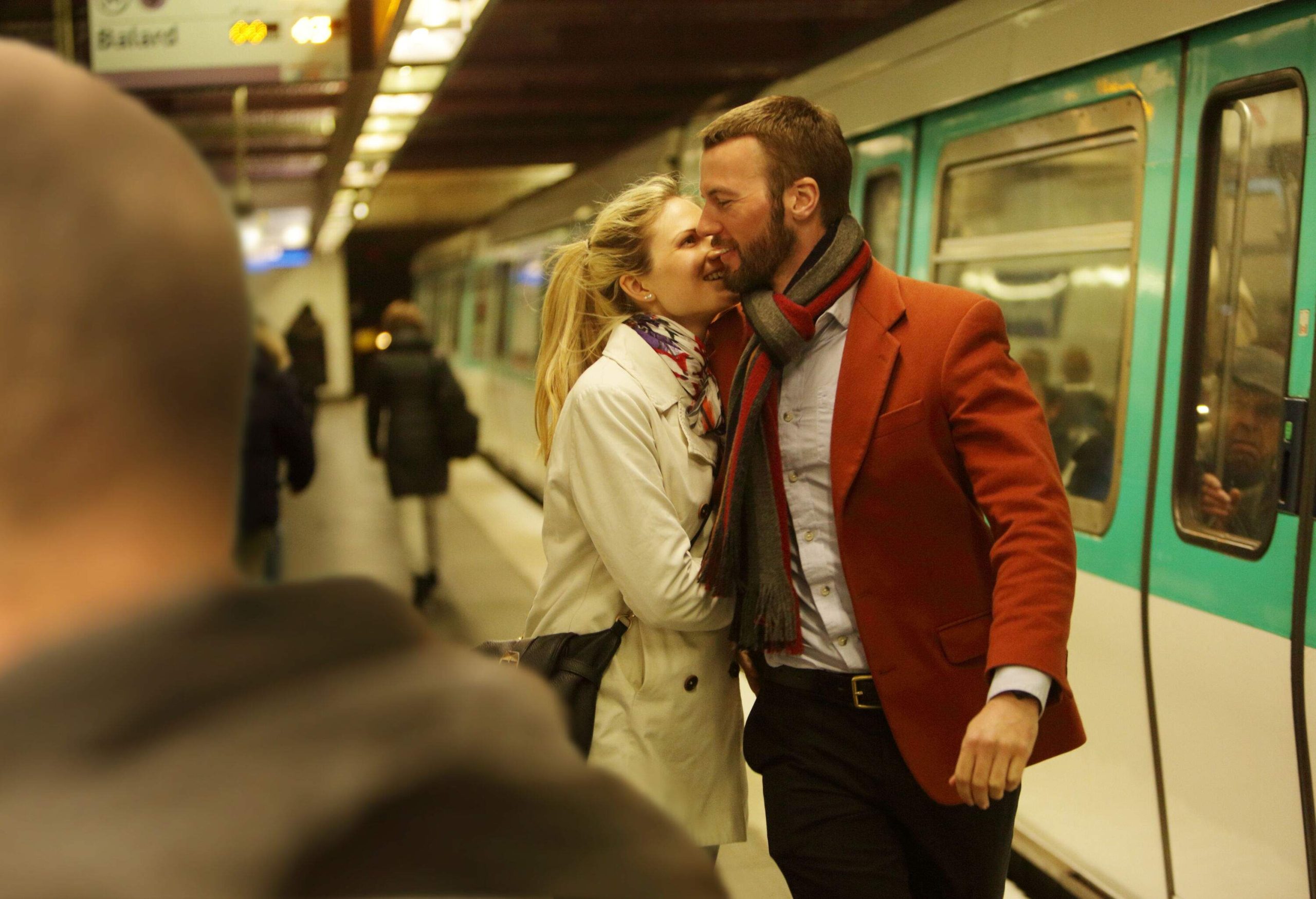 An affectionate couple standing next to a train at a metro station.