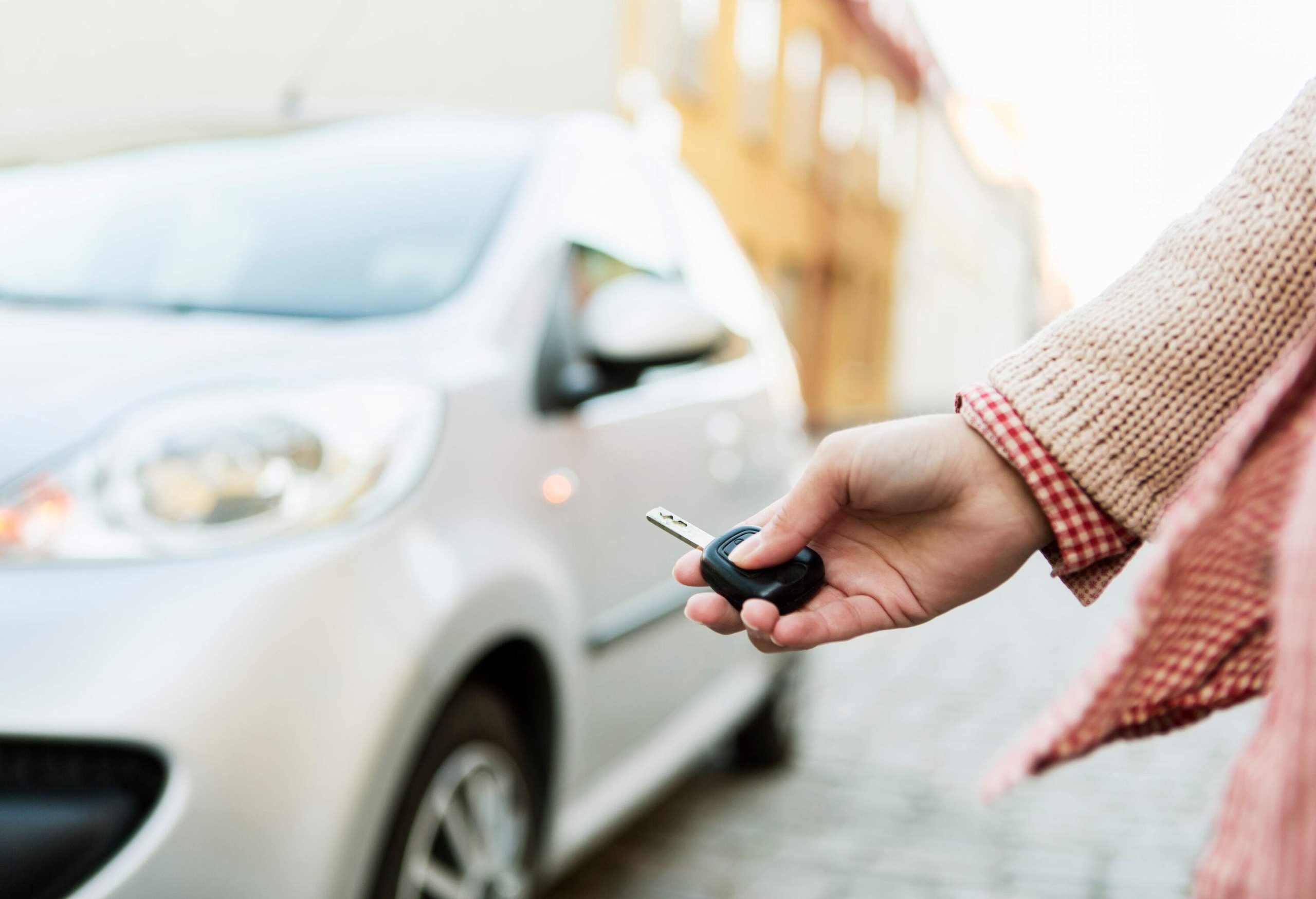 A person holds a car key against the backdrop of a white car.