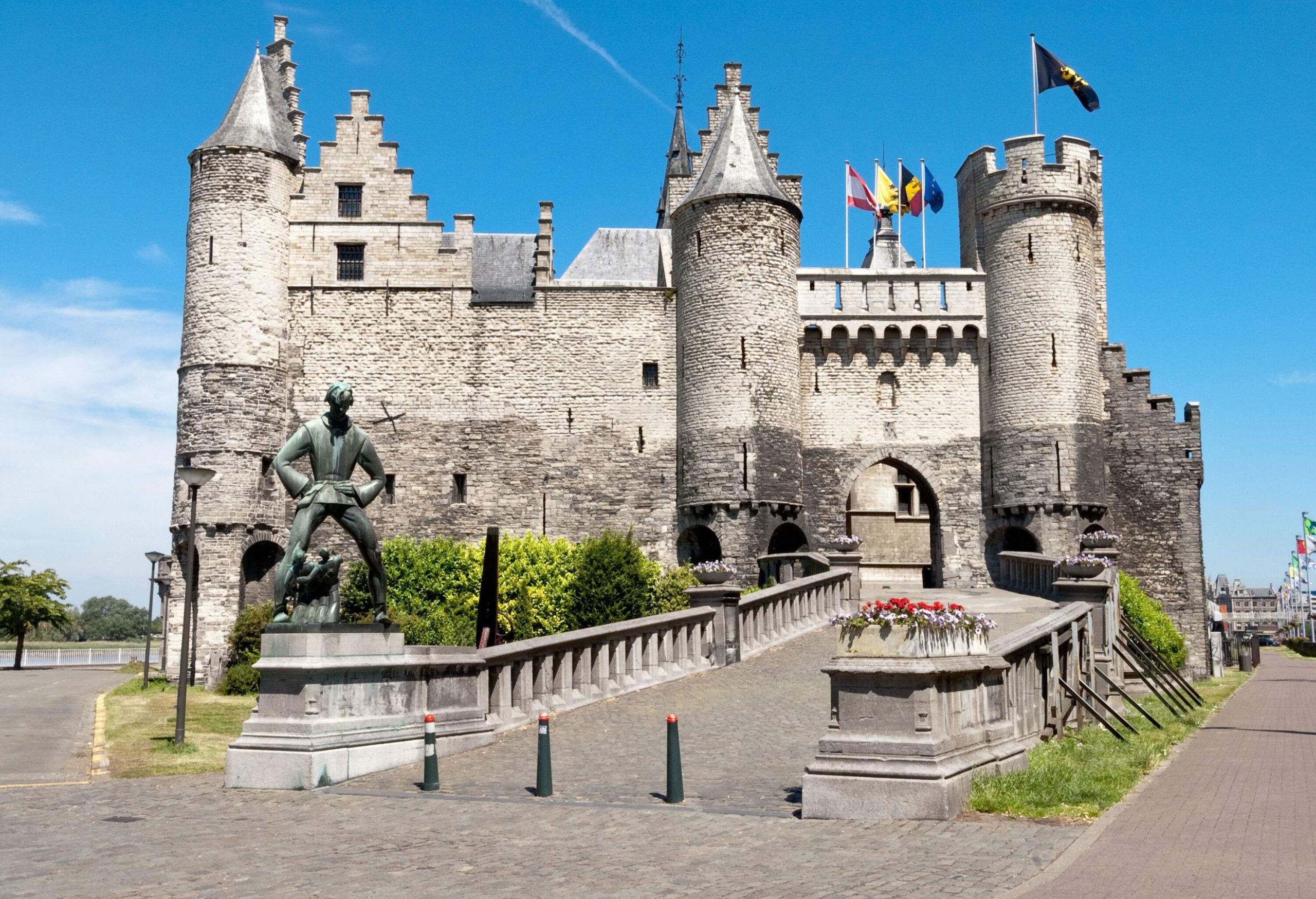 A medieval castle with flags fluttering on the rooftops and a carved figure at the end of its pathway.