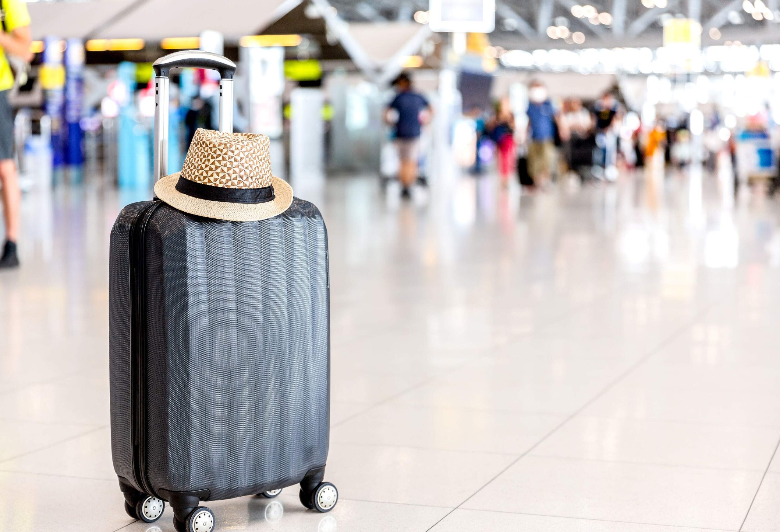 A straw hat on a suitcase standing on an airport floor.