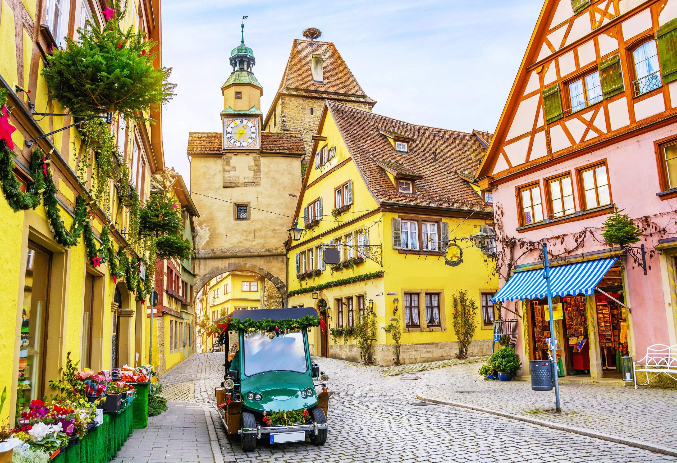 A quaint town with vibrant half-timbered buildings and a green golf cart decorated with garlands parked on the side of a paved street.