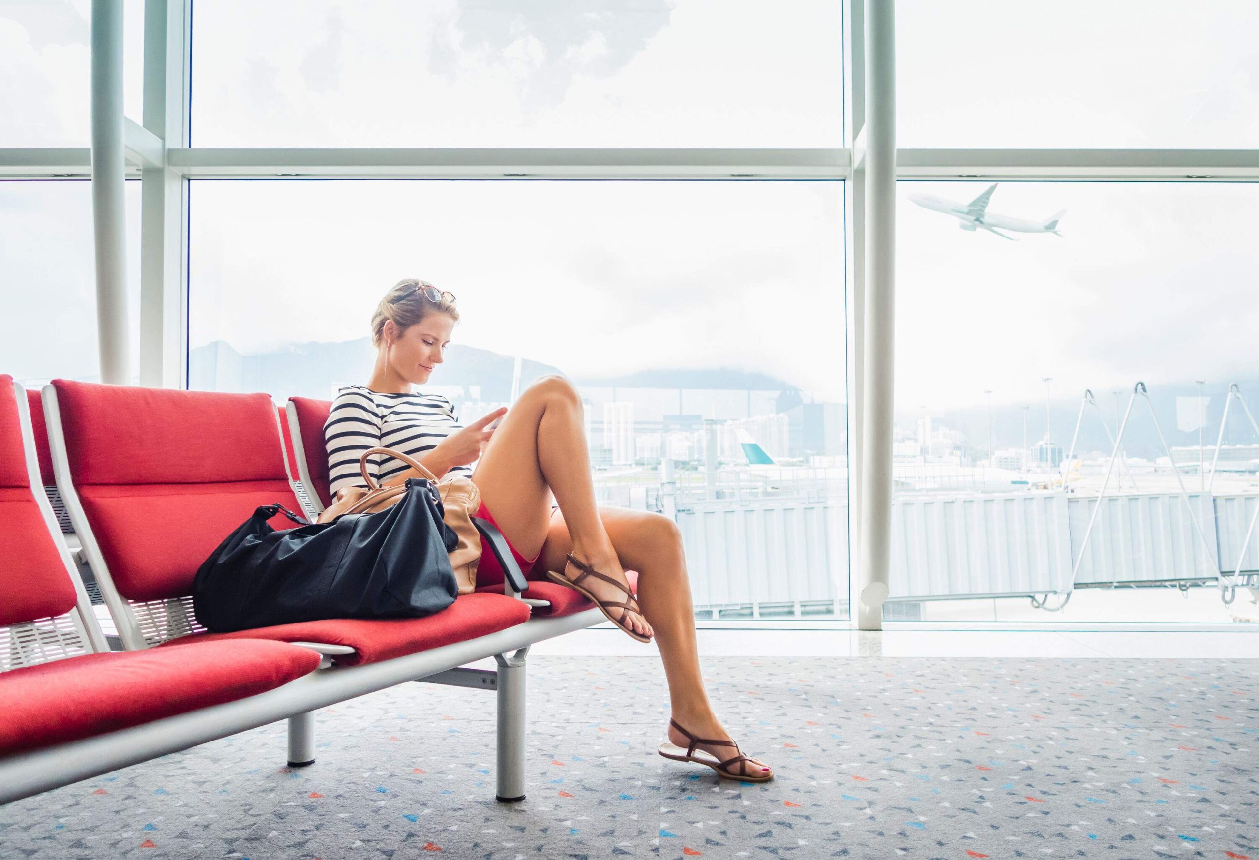 A female passenger sitting in an airport terminal, passing the time with her smartphone.