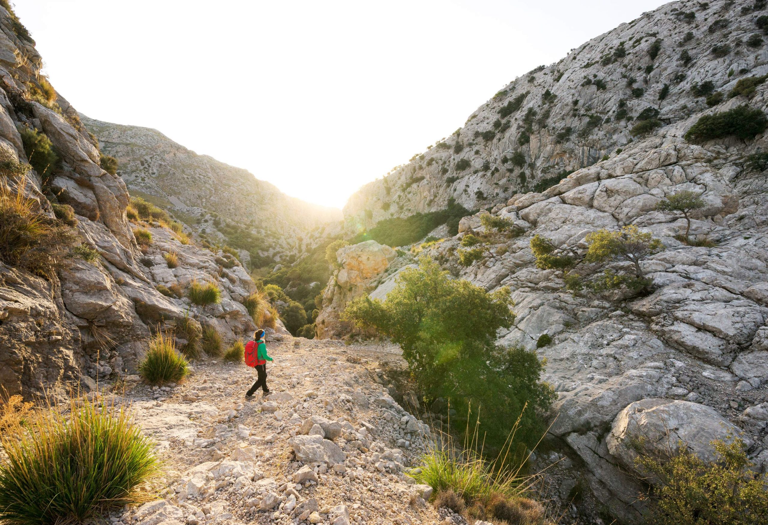 A female backpacker tramping through a rocky trail between weathered mountains.