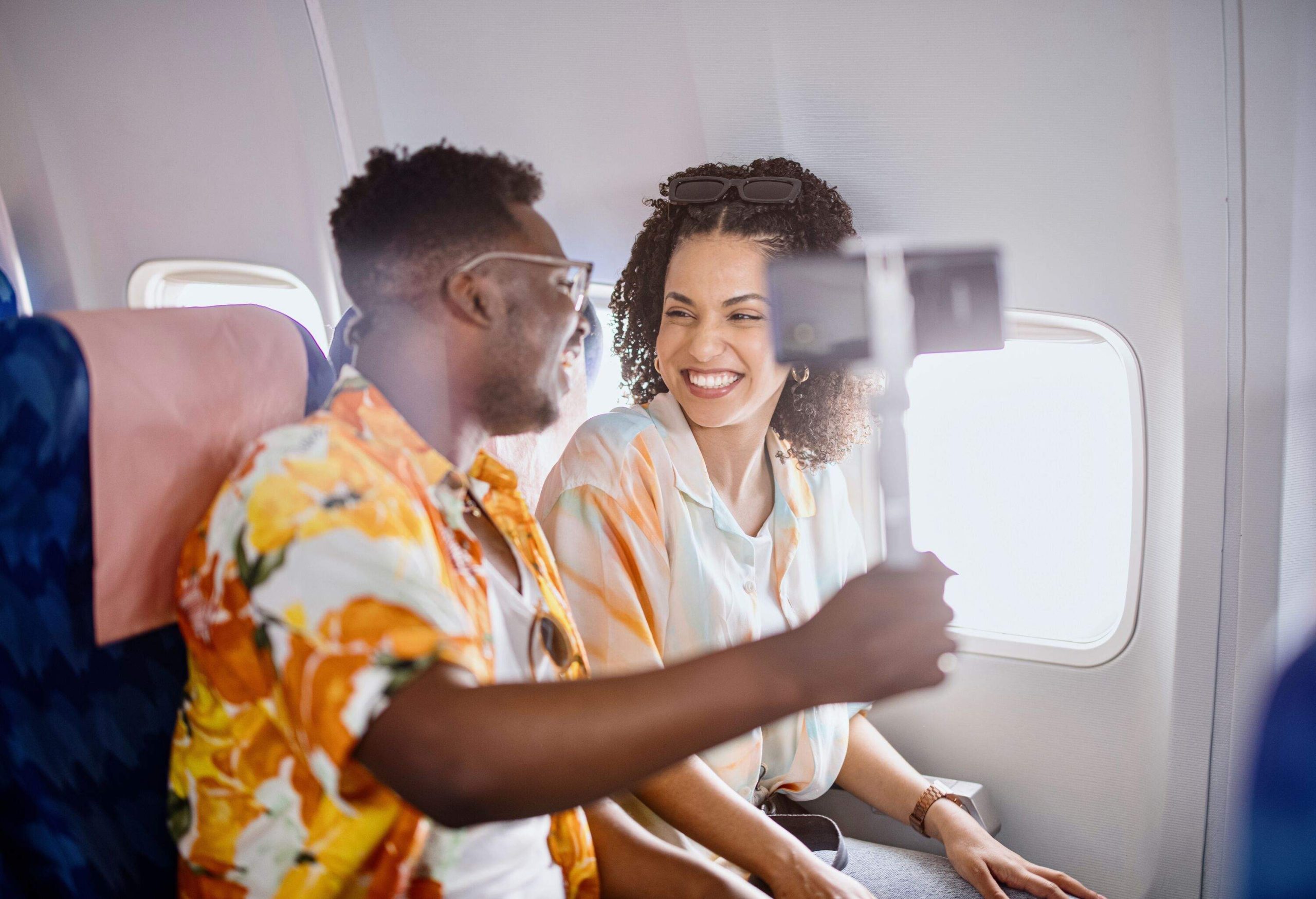 A young couple captures a memorable moment by snapping a cheerful selfie while seated together inside an airplane.