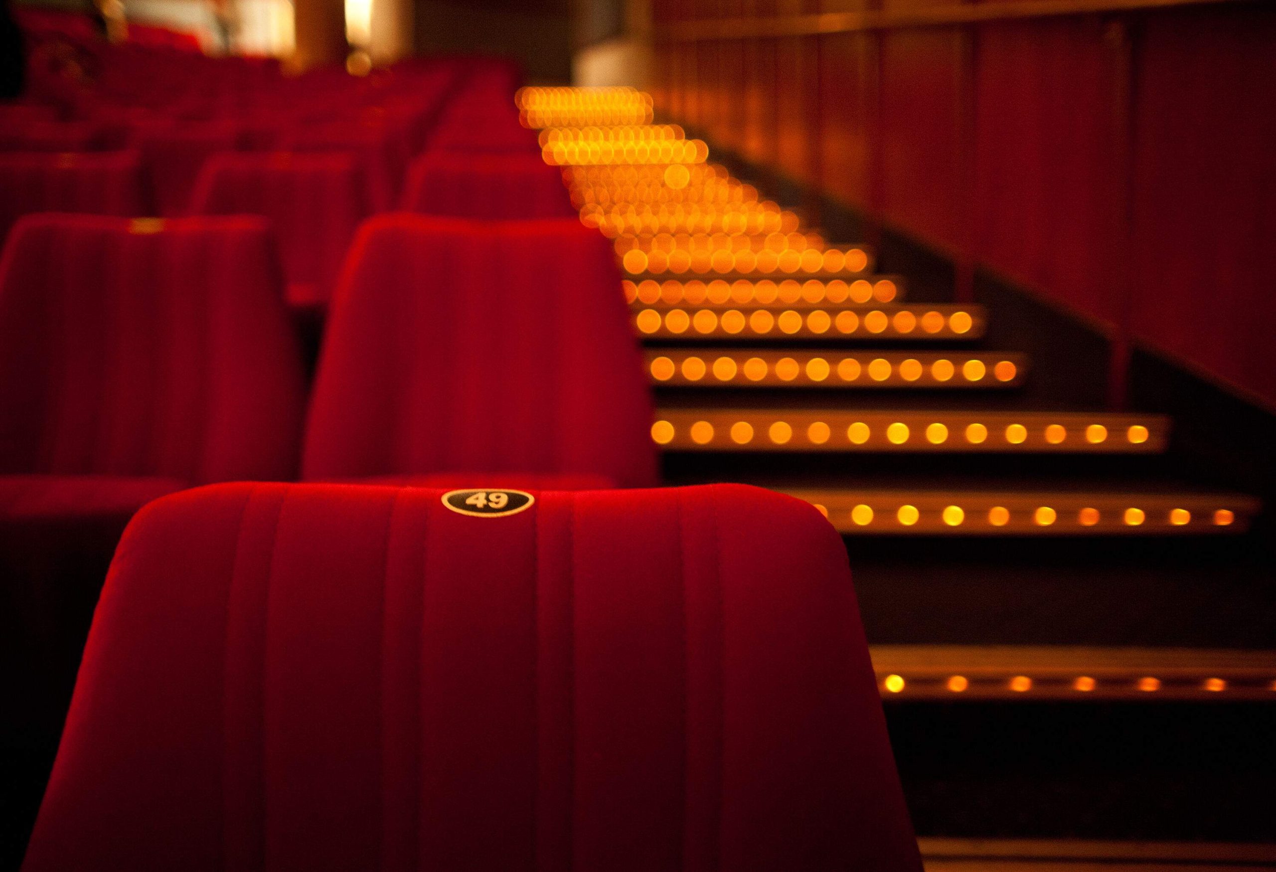 A rows of red empty seats in a theatre next to an illuminated stepped aisle.