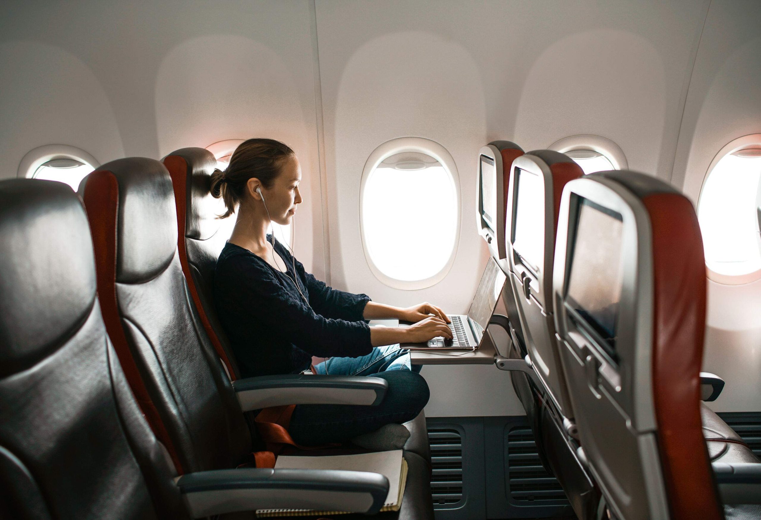 A woman seated inside an aircraft by the window engaged in her laptop.