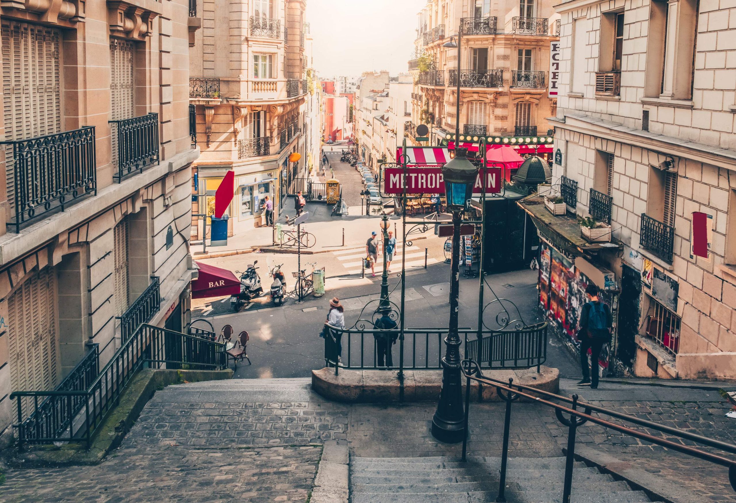 A wide staircase in the middle of two buildings alongside an asphalt road with several people around.