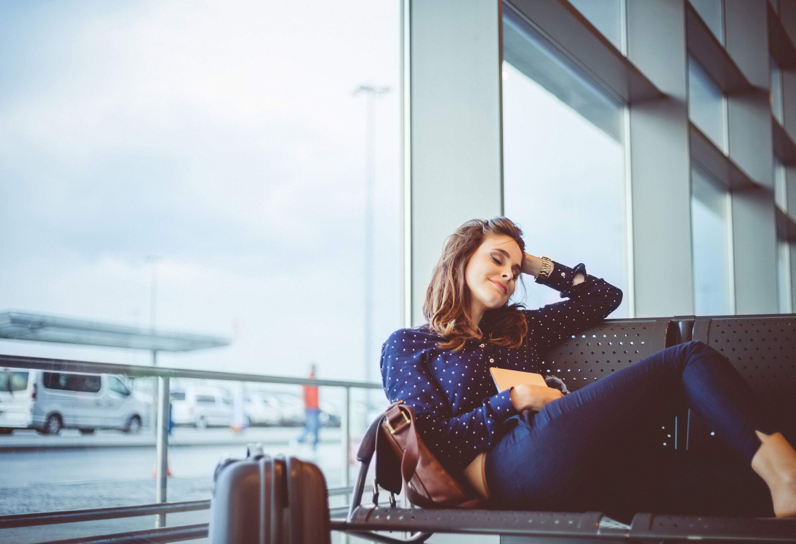 A female passenger waiting happily at a terminal as she sits comfortably in a row of chairs.