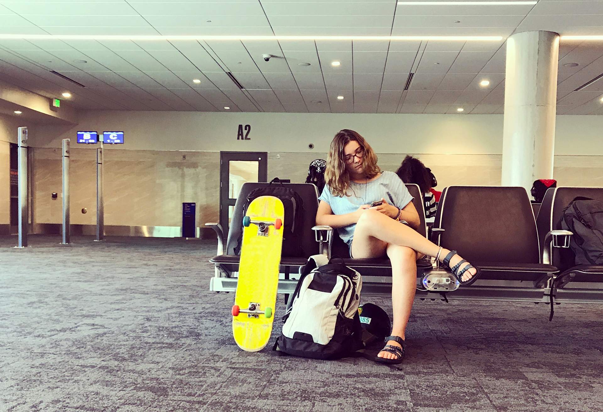 Woman waiting for flight at airport with small backpack and skateboard
