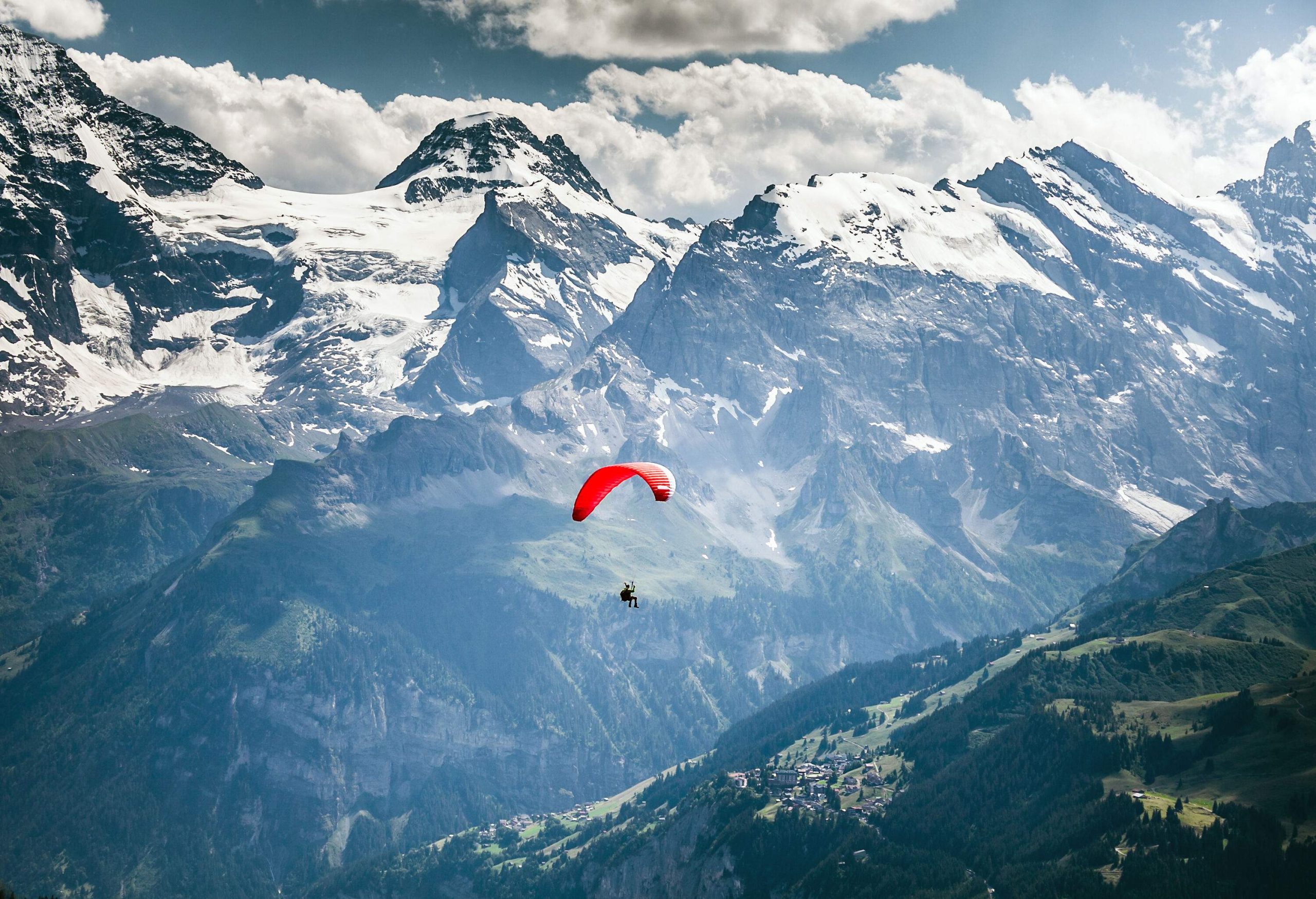 A person paragliding over the rugged snow-capped mountains.