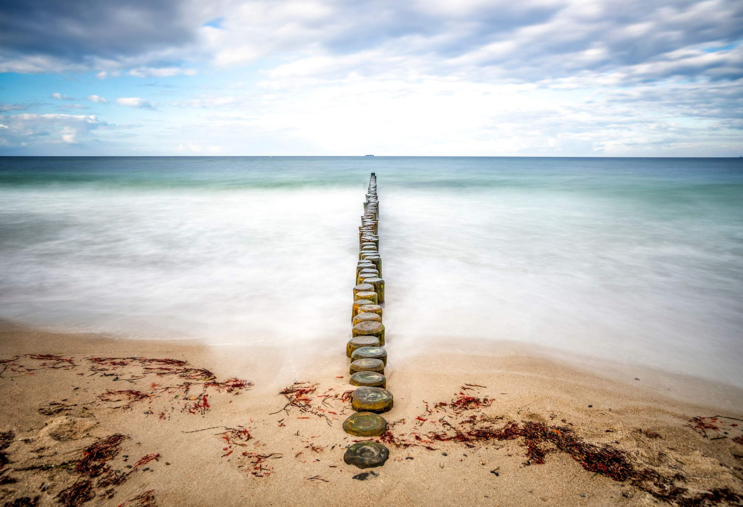 A line of wooden groynes stretching from the shore all the way to the sea.