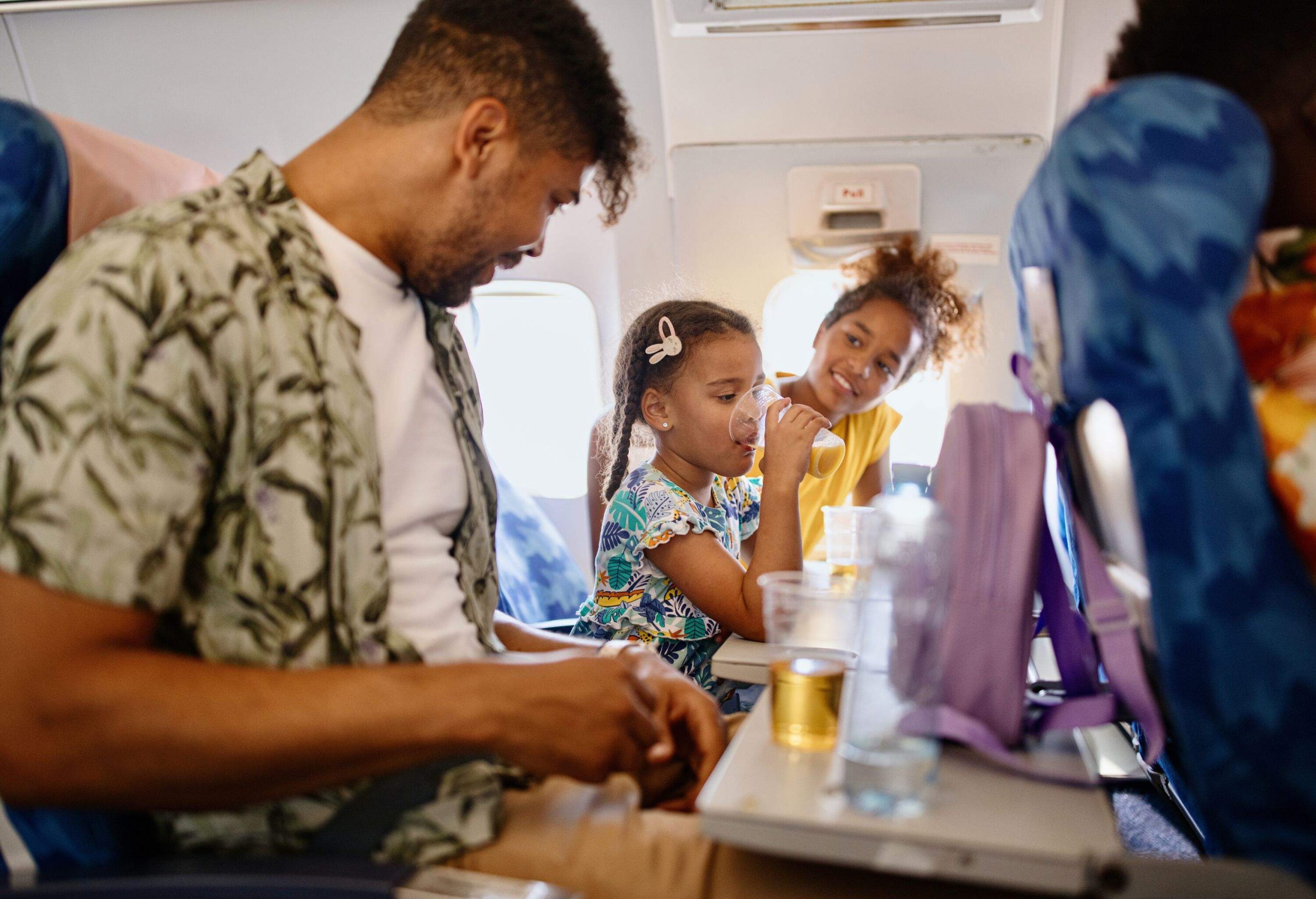 A man and two young girls having drinks on a plane.