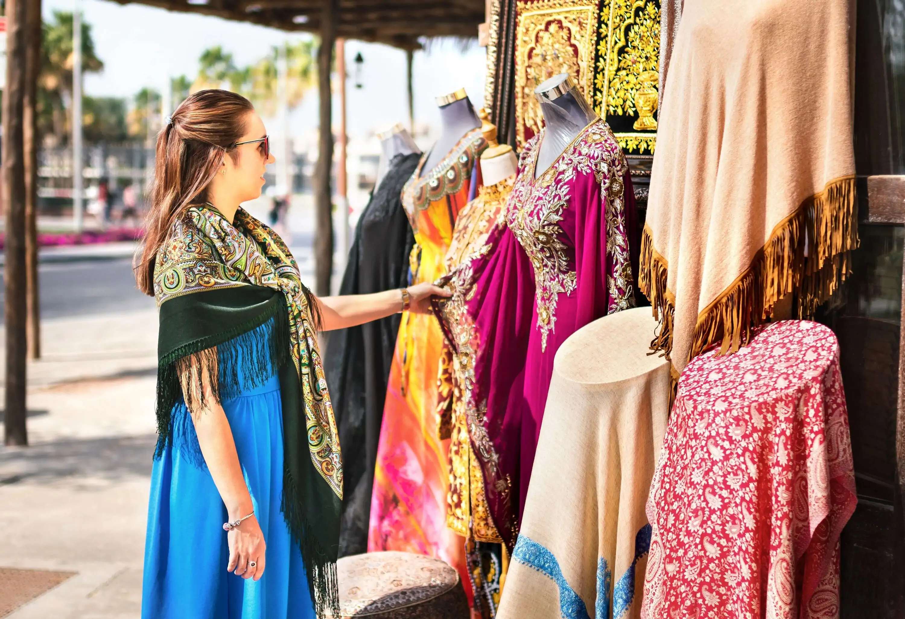 A tourist browses the racks of an outdoor store selling traditional Arabian clothing.