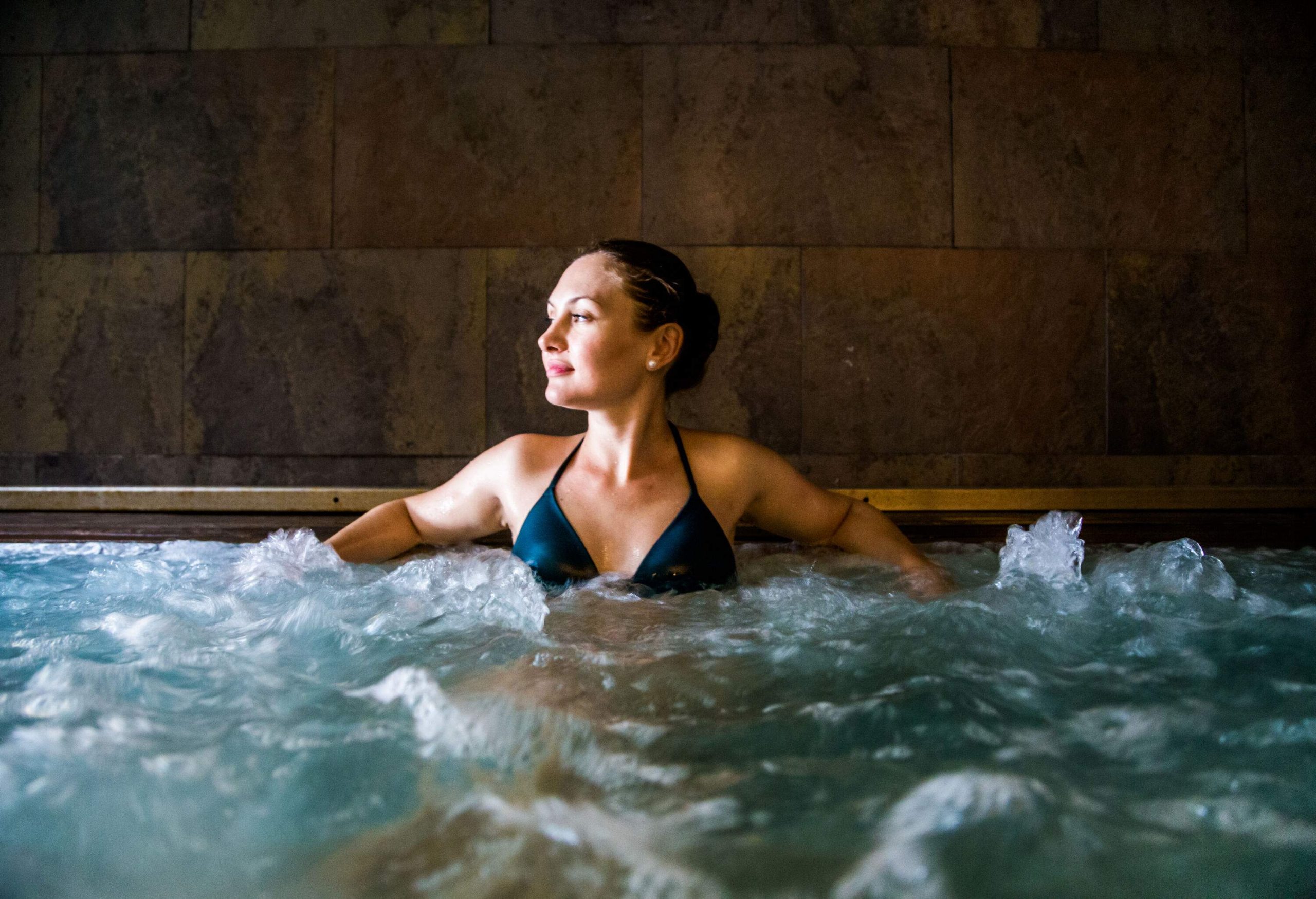 A woman leaning back against the edge of a jacuzzi, her body relaxed by the jetted water.