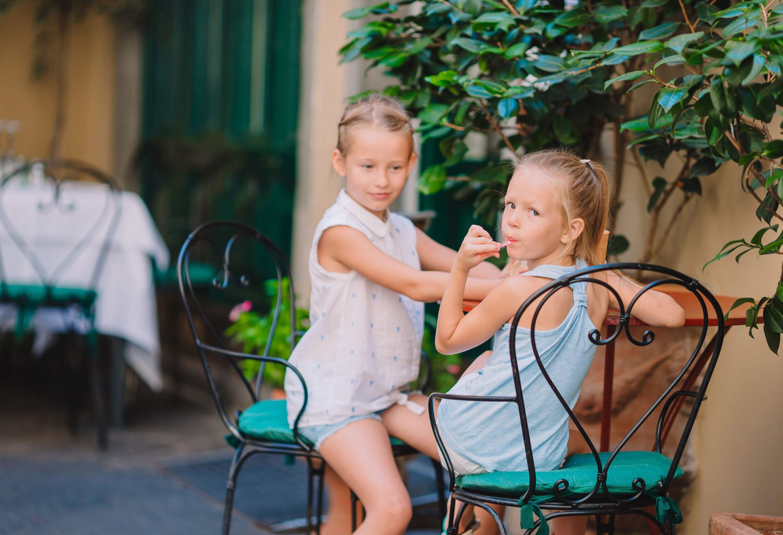 Two girls eat their ice cream at a table outdoors.