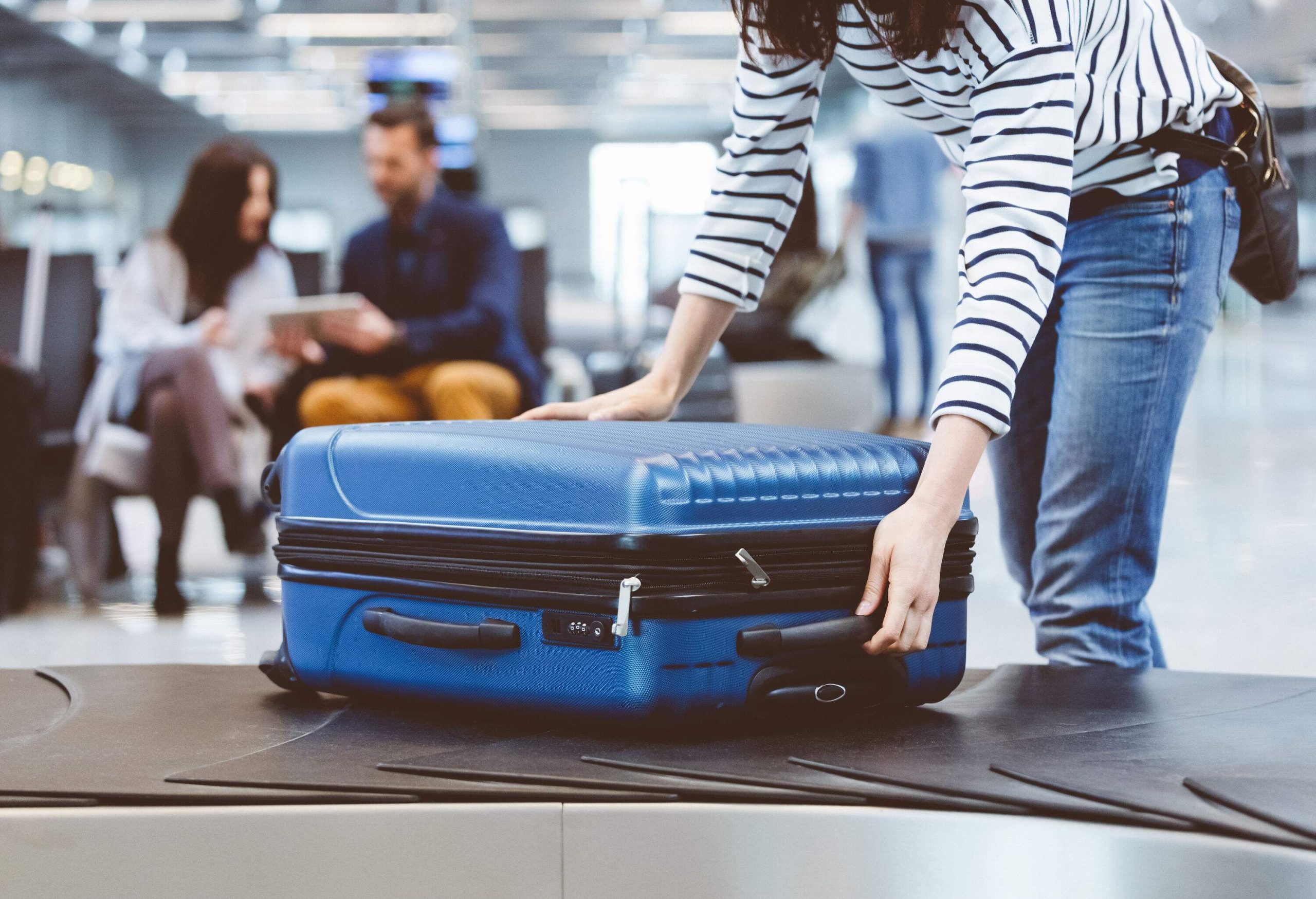 Young woman passenger collecting her luggage from conveyor belt. Female traveler picking up suitcase from baggage claim line in airport terminal.